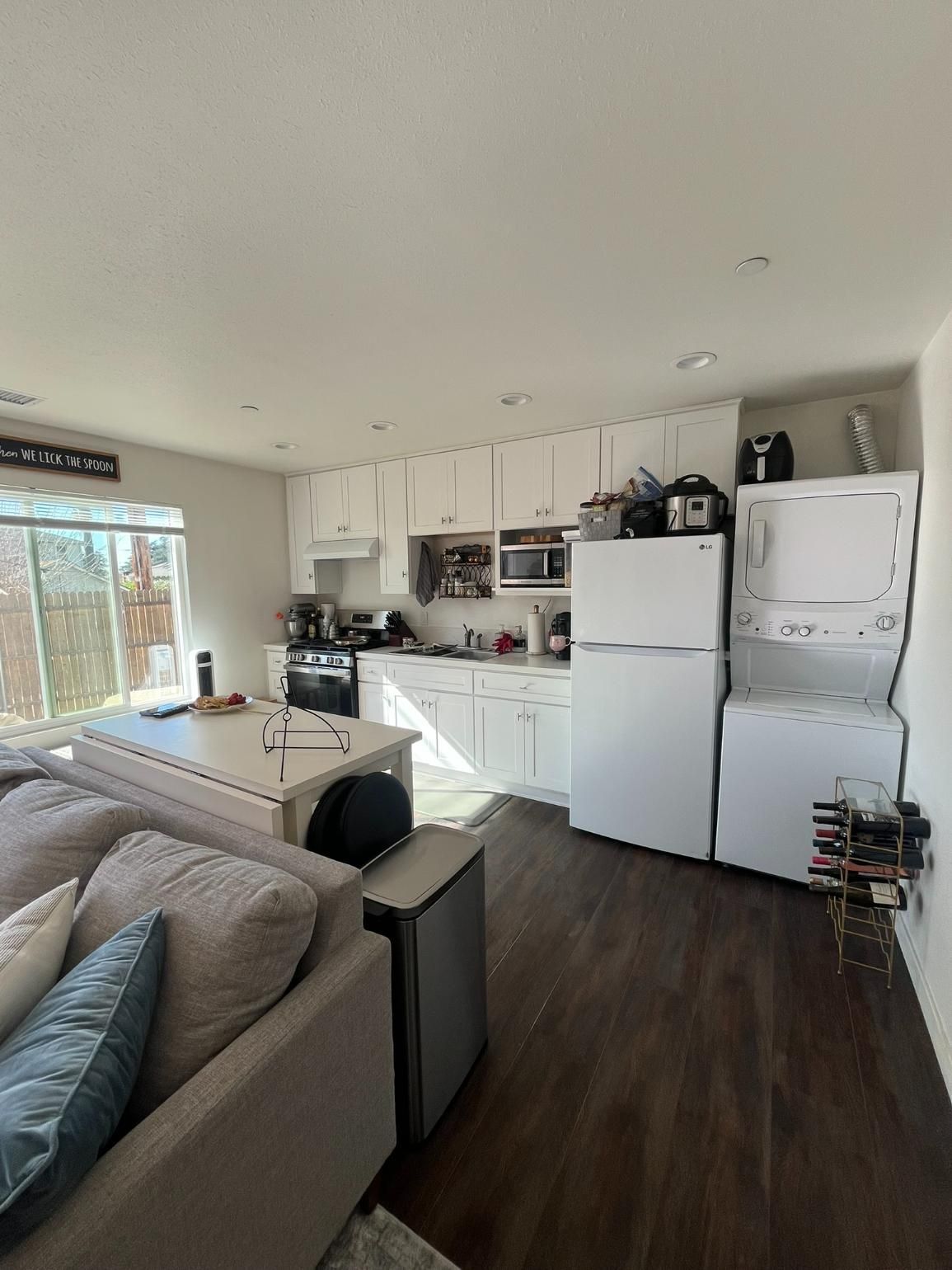 Bright living room with white kitchen, refrigerator, sofa, and dark wood flooring