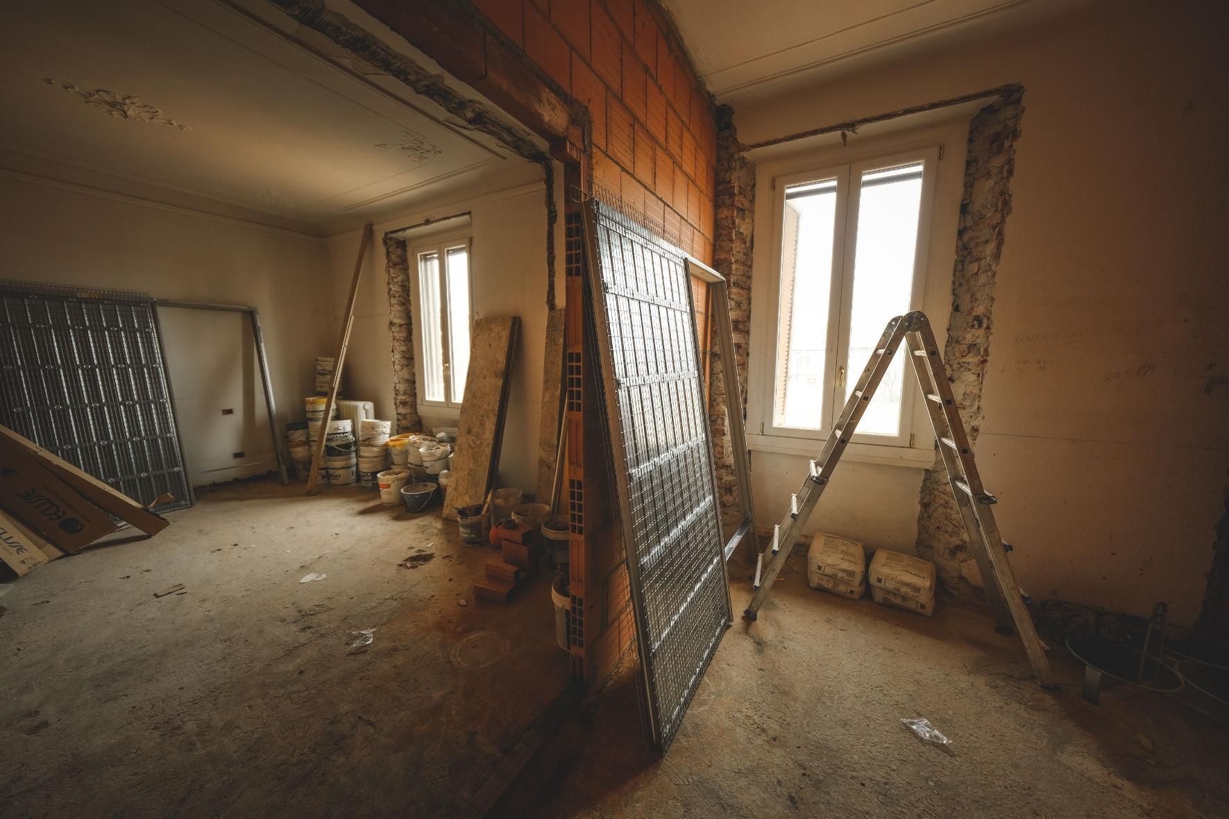 Renovation site with ladders, tools, and exposed brick walls in a dusty room