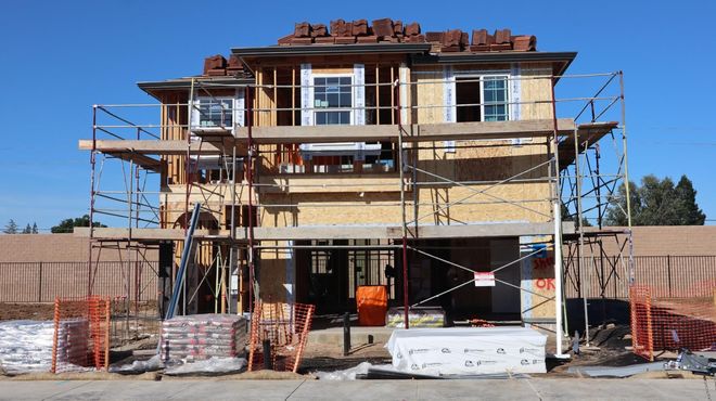 Three-story house under construction with scaffolding and exposed framing