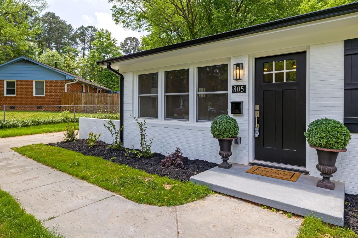 Modern white house exterior with black door, potted shrubs, and concrete walkway