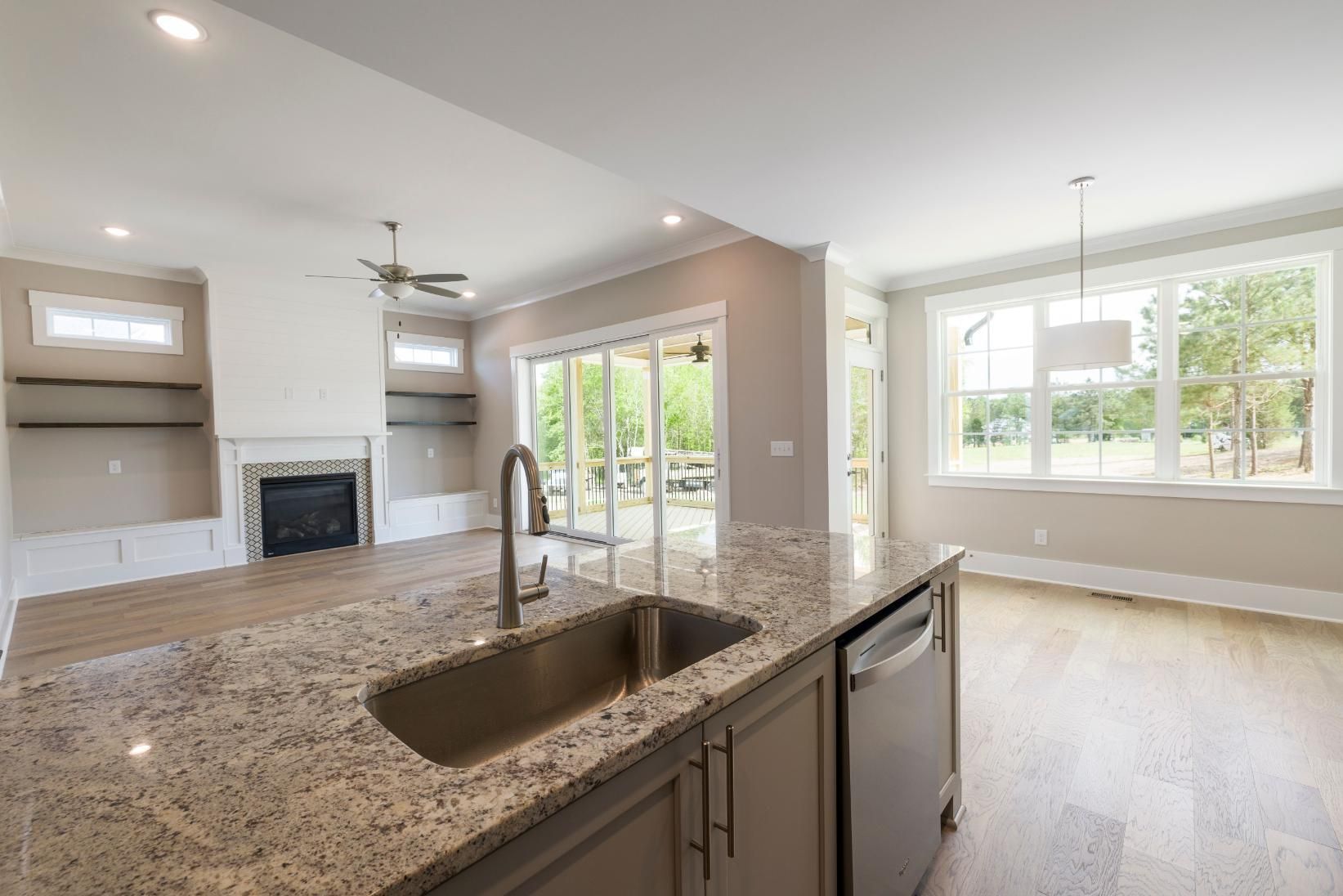 Modern kitchen with granite island, built-in sink, fireplace, and bright open dining area with large windows