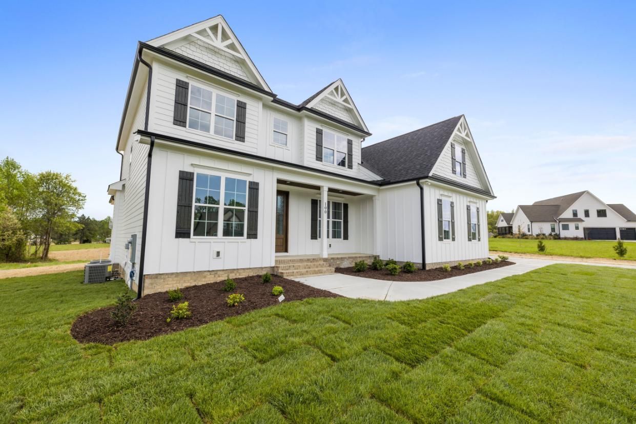 White two-story suburban house with dark roof, large windows, and green lawn under a blue sky