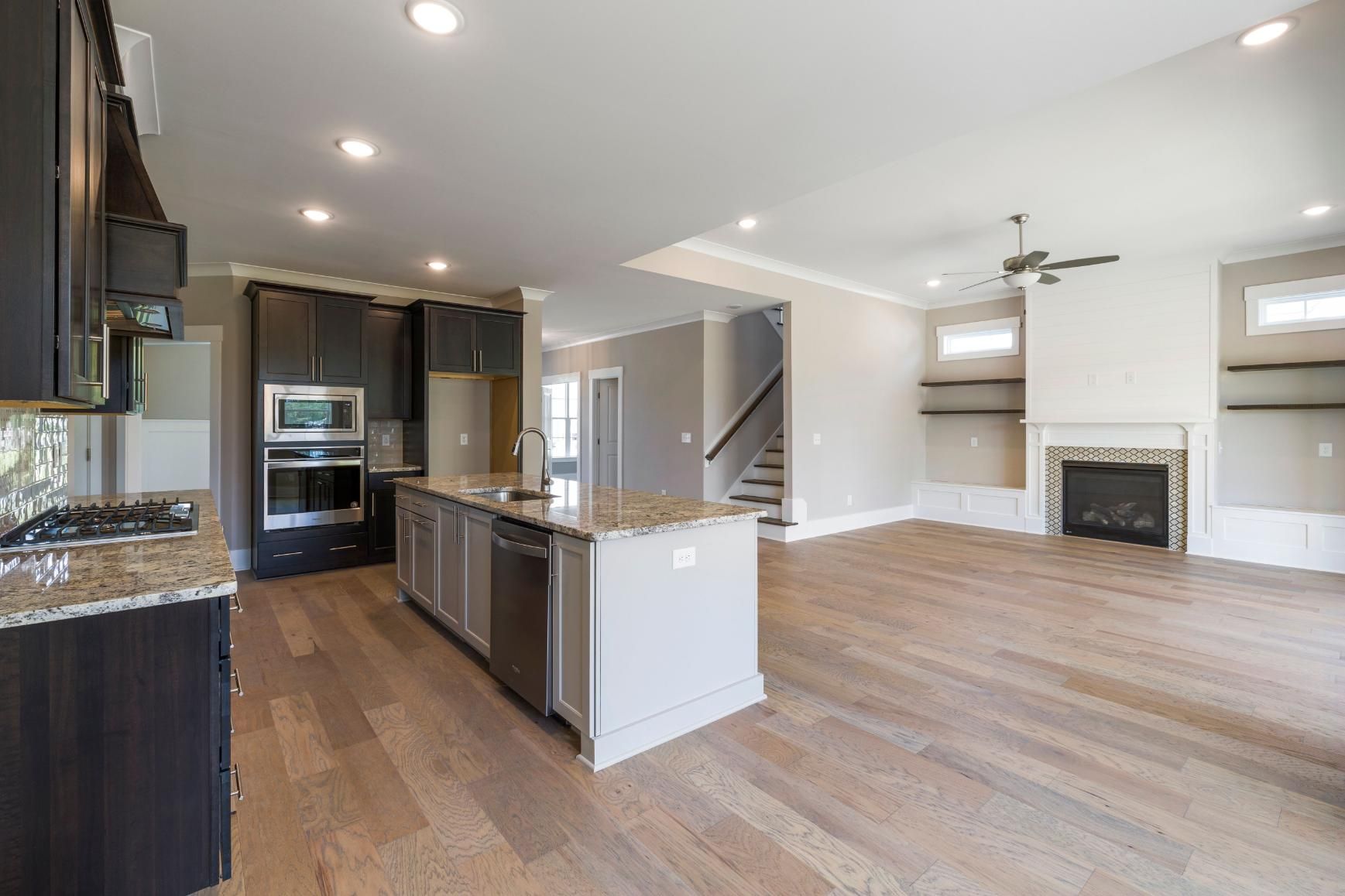 Modern open-concept kitchen and living room with dark cabinets, wood floors, and a fireplace