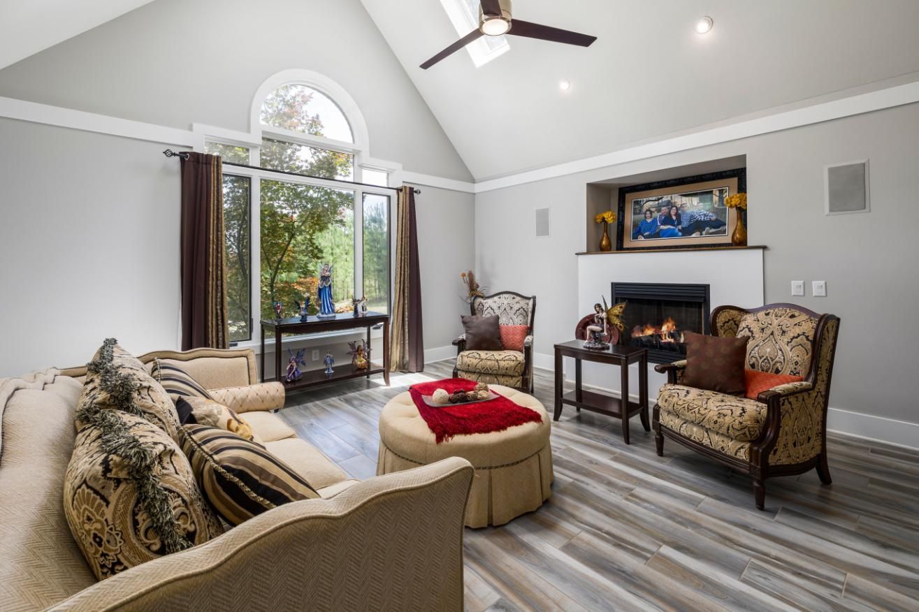 Bright living room with beige sofas, patterned chairs, a fireplace, and tall arched windows.