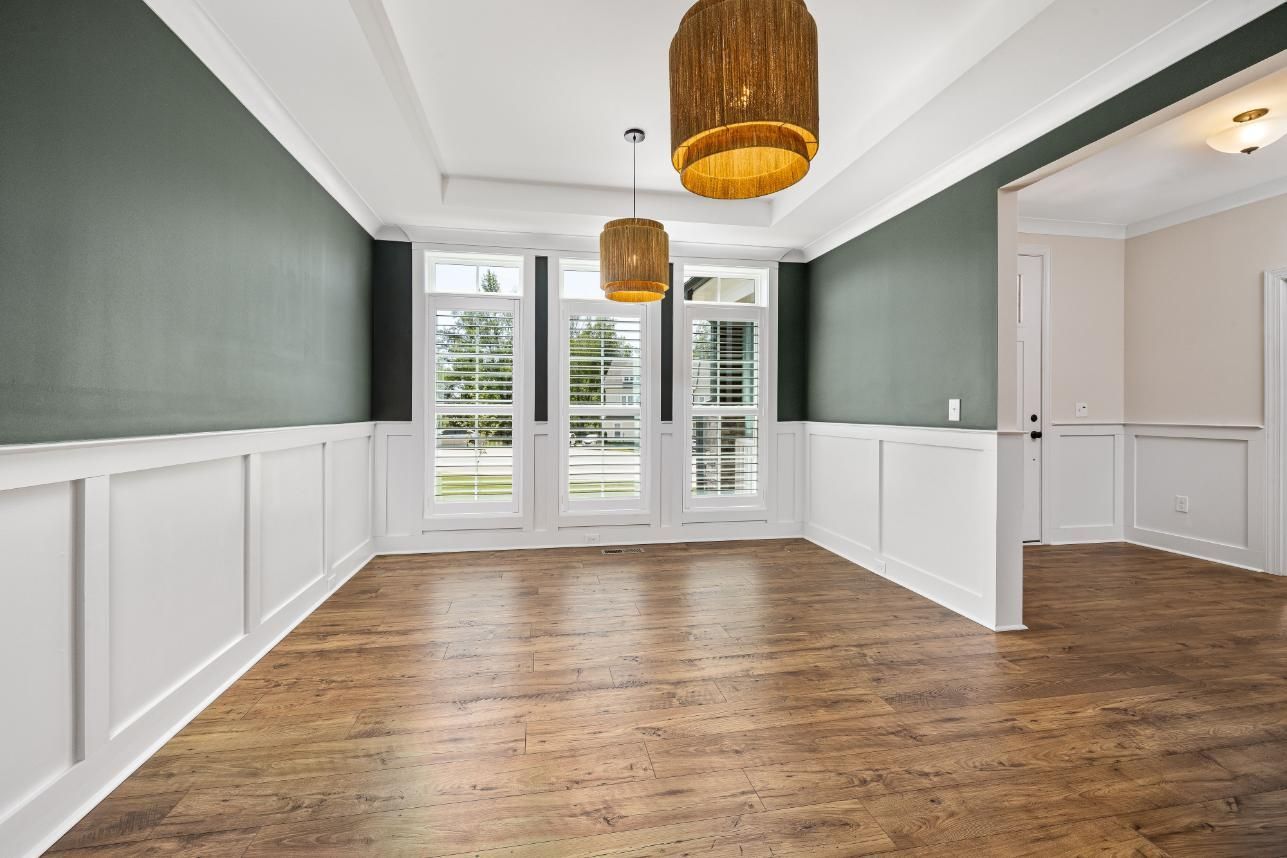 Empty dining room with wood floors, green walls, white wainscoting, and French doors leading outside.