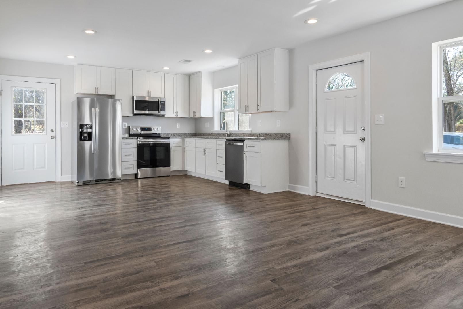Bright open kitchen and living area with white cabinets, dark wood floors, and stainless steel appliances