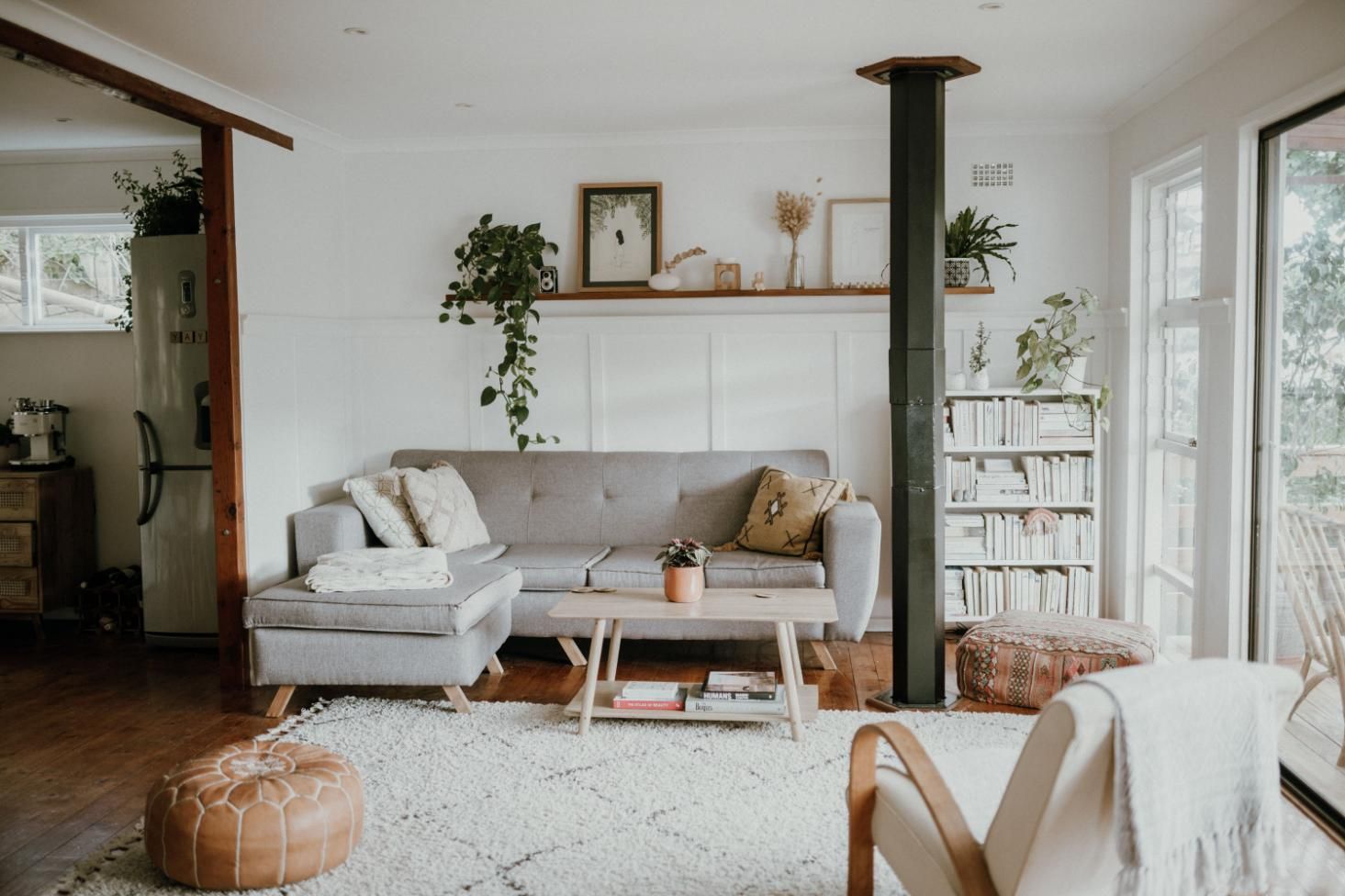 Bright living room with gray sofa, wooden shelves, plants, and large windows overlooking a balcony