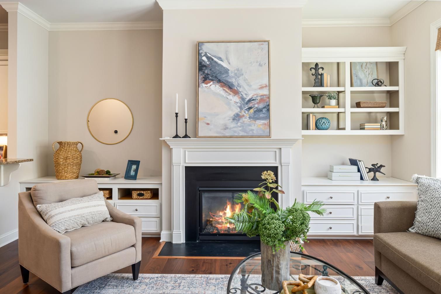 Cozy living room with fireplace, beige chairs, white built-ins, and abstract art above the mantel