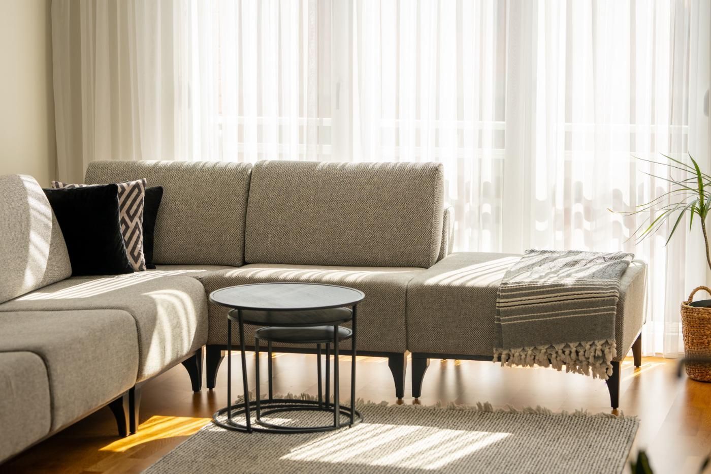 Bright living room with a gray sectional sofa, round coffee table, and sunlight through sheer curtains.