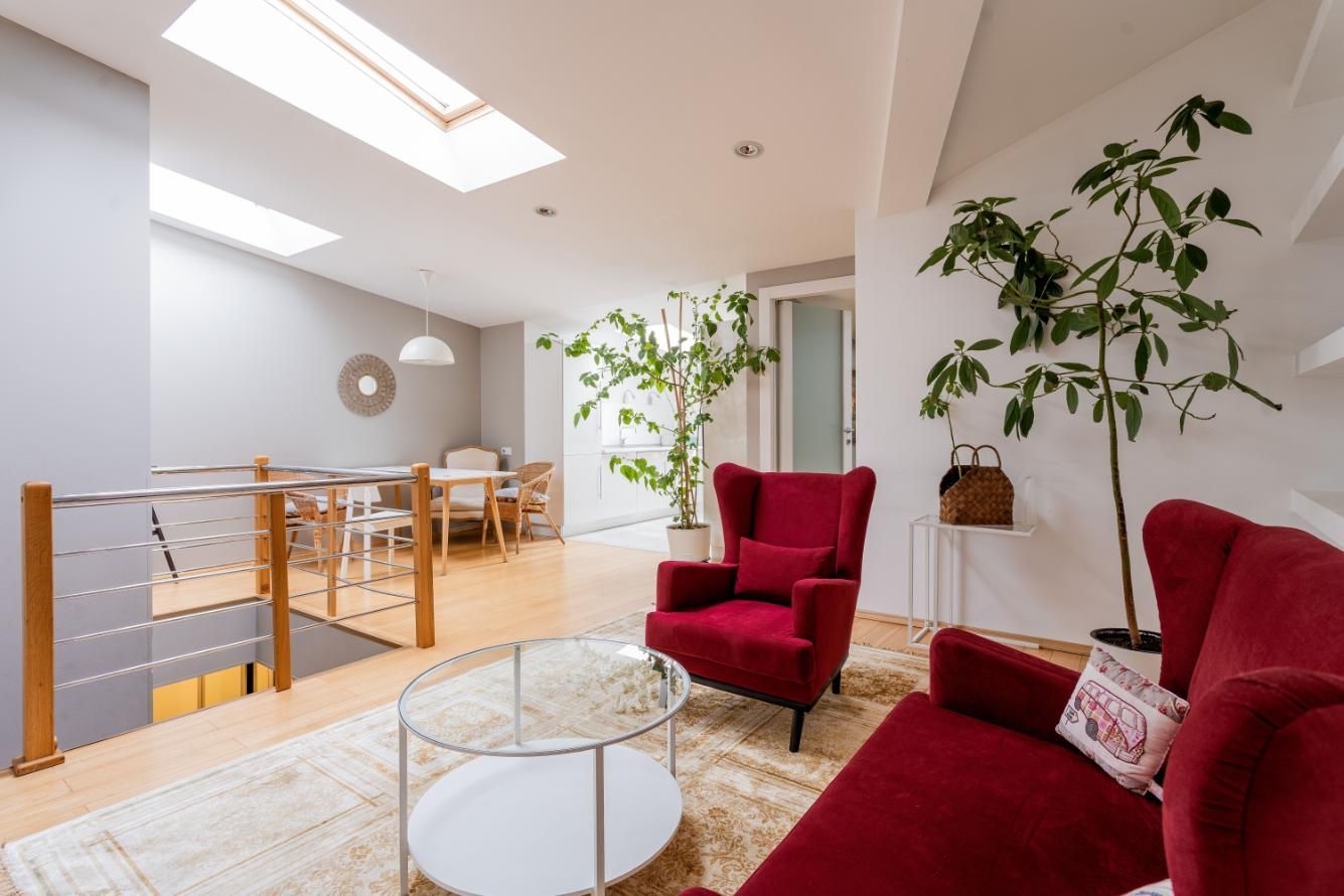 Bright modern loft living room with red chairs, glass coffee table, skylights, and indoor plants