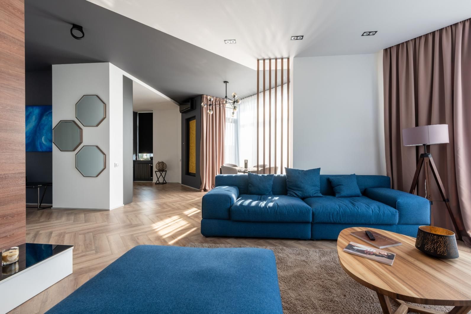 Modern living room with blue sectional sofa, wood floor, and floor-to-ceiling curtains