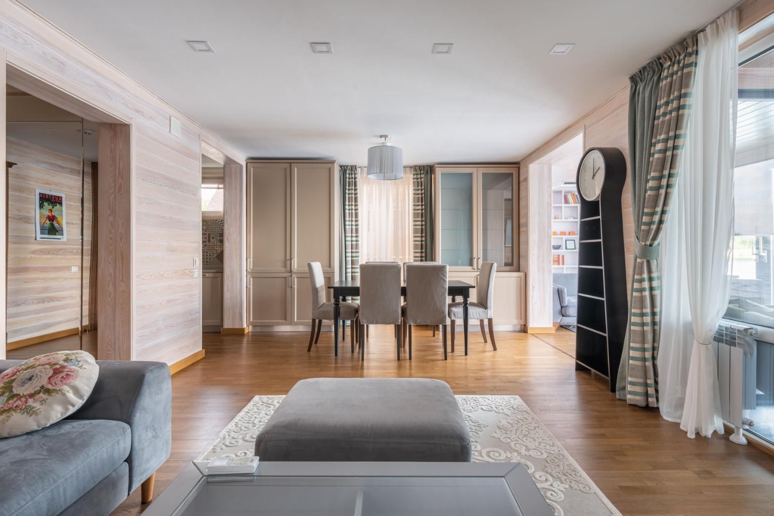 Bright modern dining room with a table, chairs, gray sofa, wood floors, and tall windows with curtains