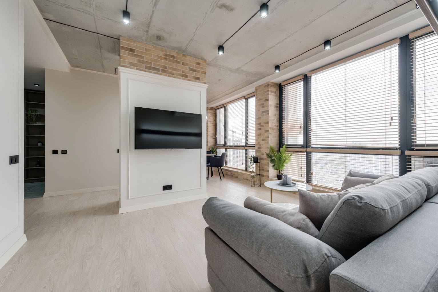 Modern living room with gray sectional, wall-mounted TV, tall windows, and light wood floors