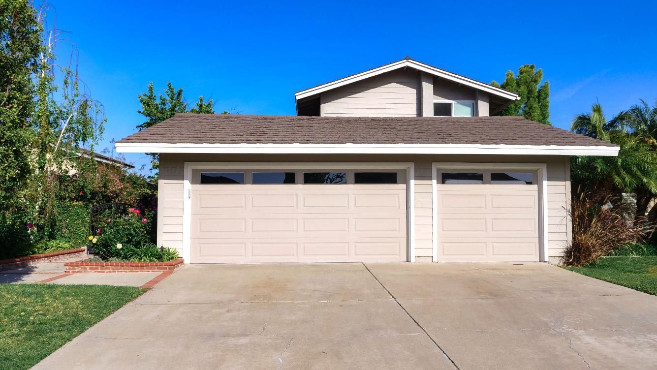 Suburban two-car garage with beige doors, concrete driveway, and blue sky