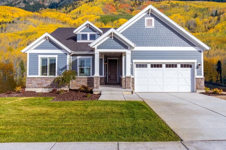 Gray suburban house with white trim, two-car garage, and autumn trees in the background