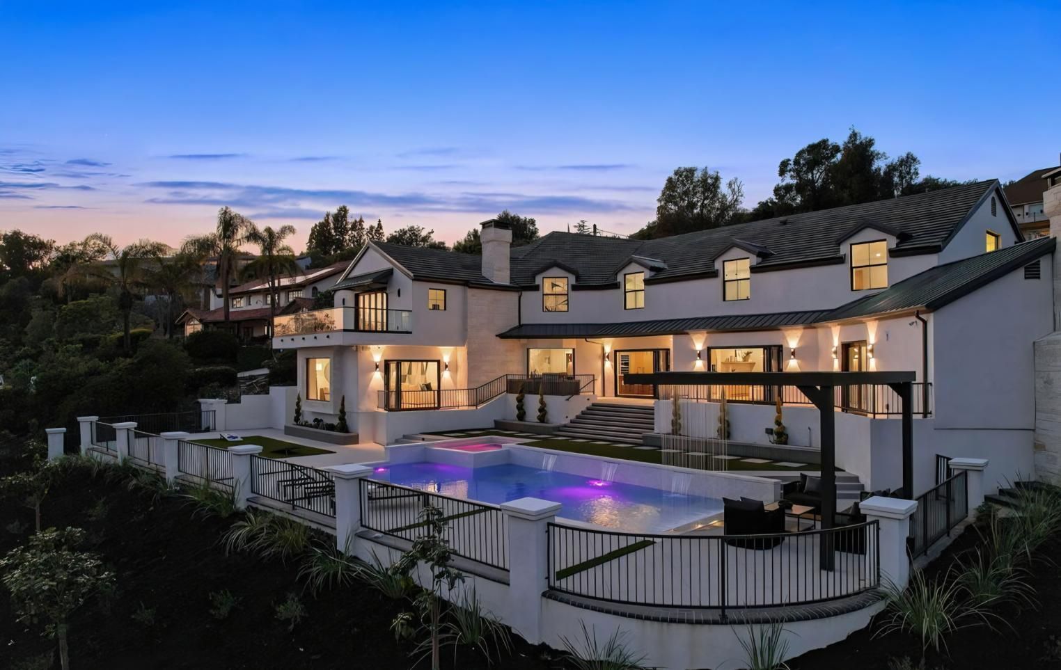 Luxurious hillside home at dusk with lit windows and a glowing backyard pool