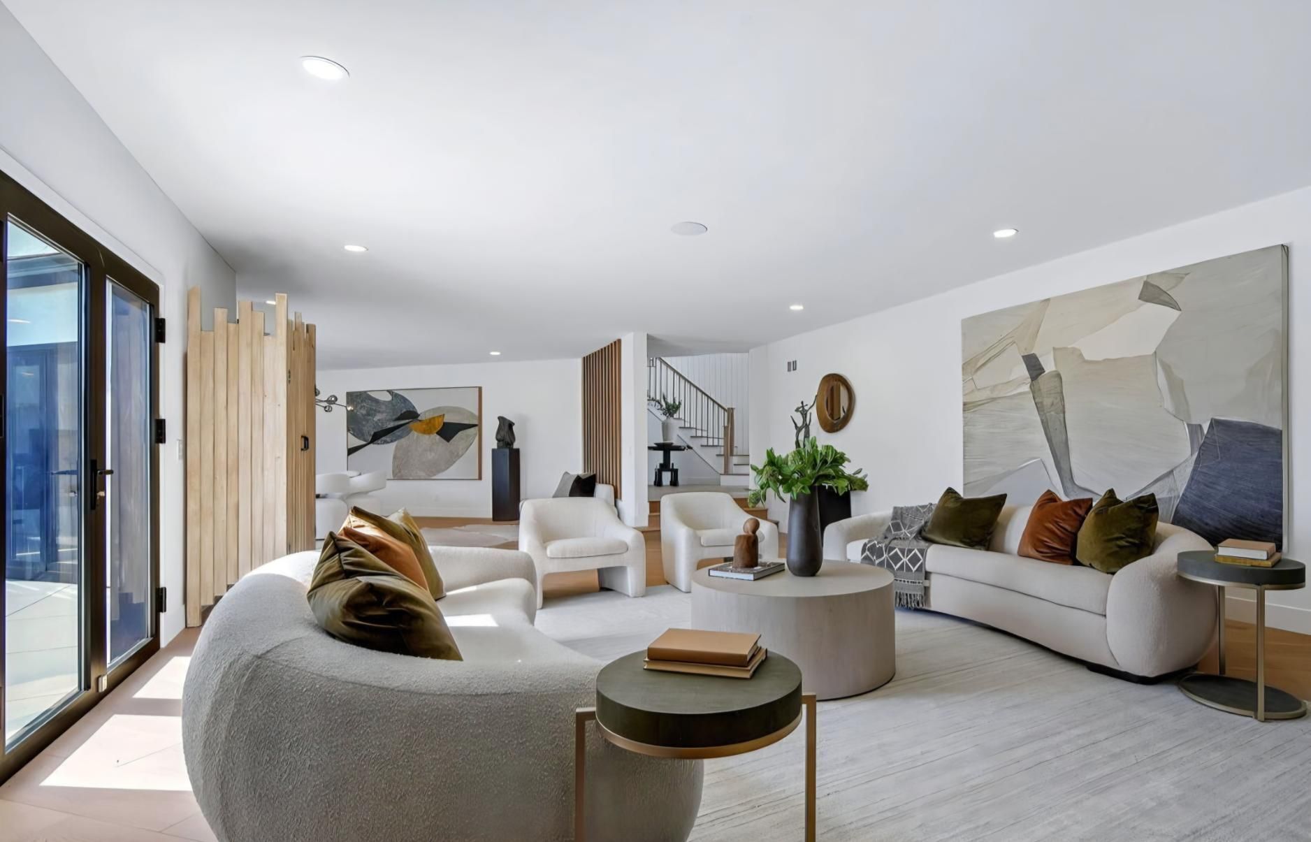 Bright modern living room with curved sofa, neutral decor, large windows, and abstract wall art