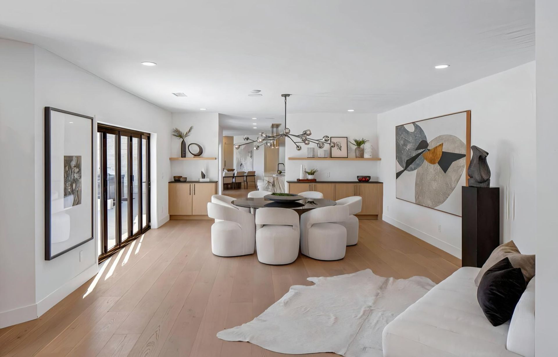 Bright modern open-plan dining and living room with white walls, round table, and abstract wall art