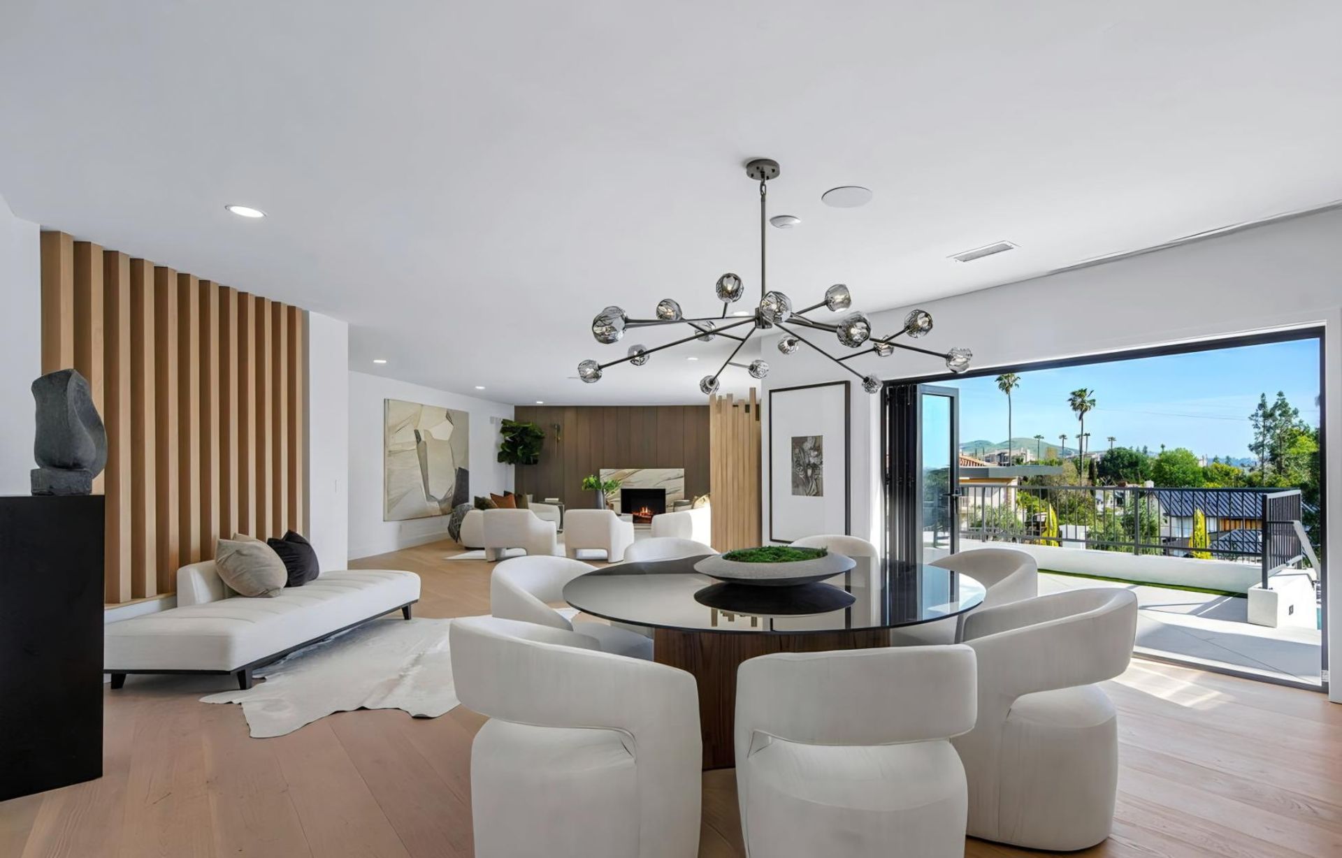 Modern open-plan living room with white furniture, round dining table, and large sliding glass doors to a patio.