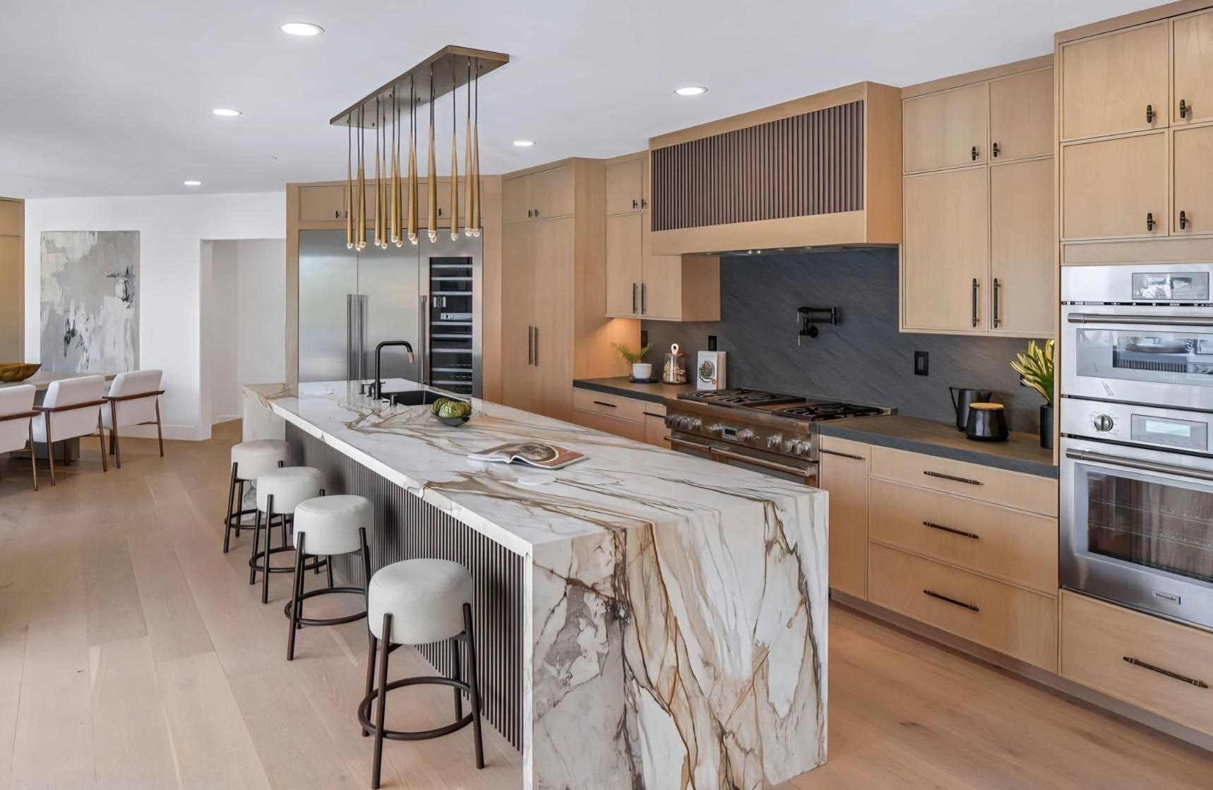 Modern kitchen with a marble island, light wood cabinets, and pendant lights