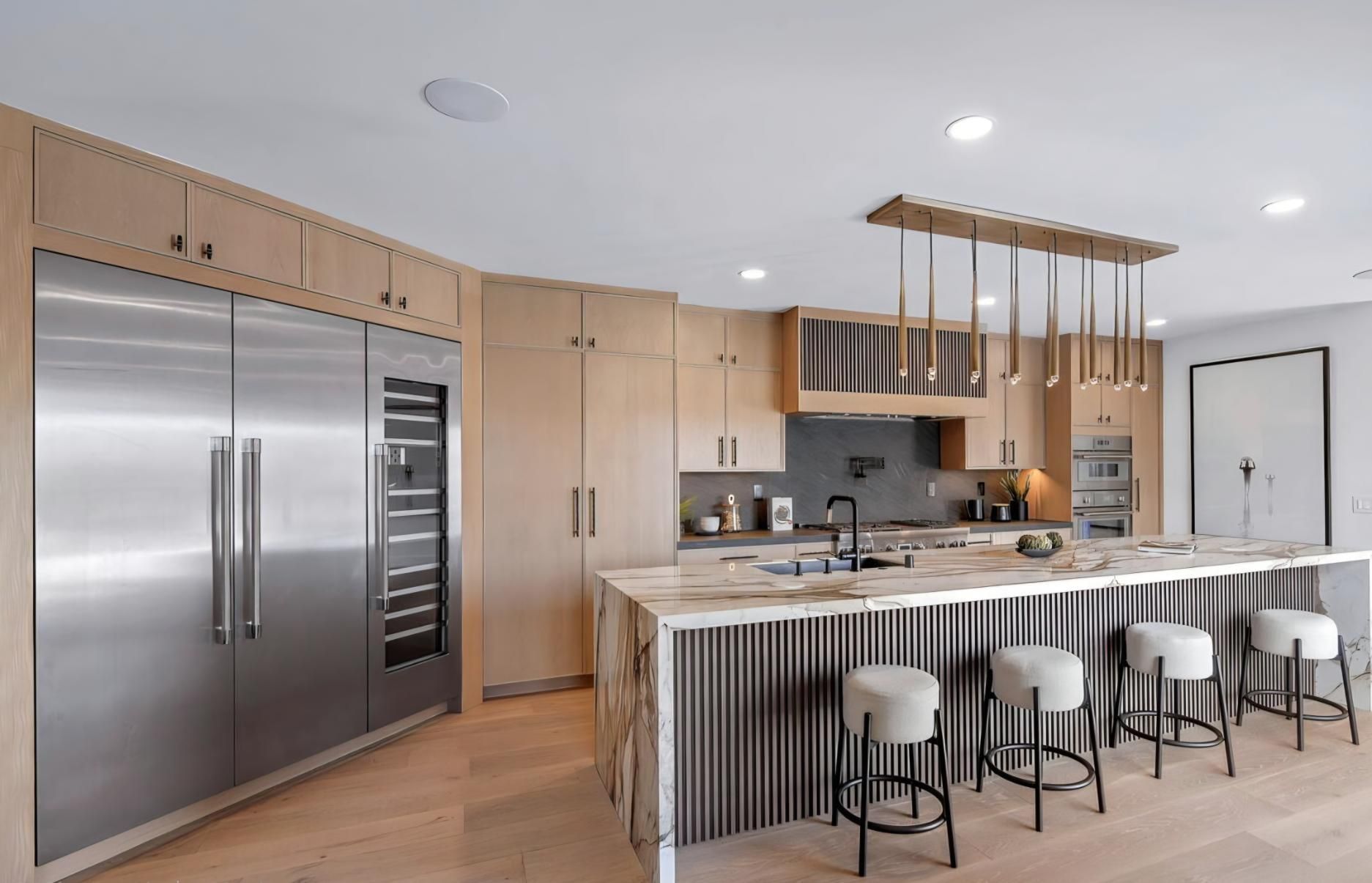 Modern kitchen with stainless steel appliances, light wood cabinets, and a marble island with bar stools