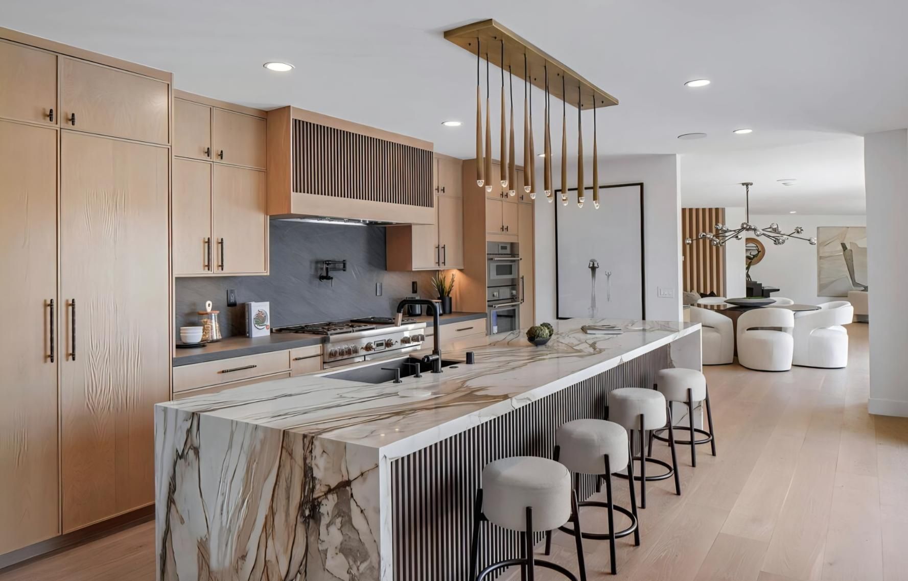 Modern kitchen with marble island, pendant lights, and light wood cabinetry in an open living space