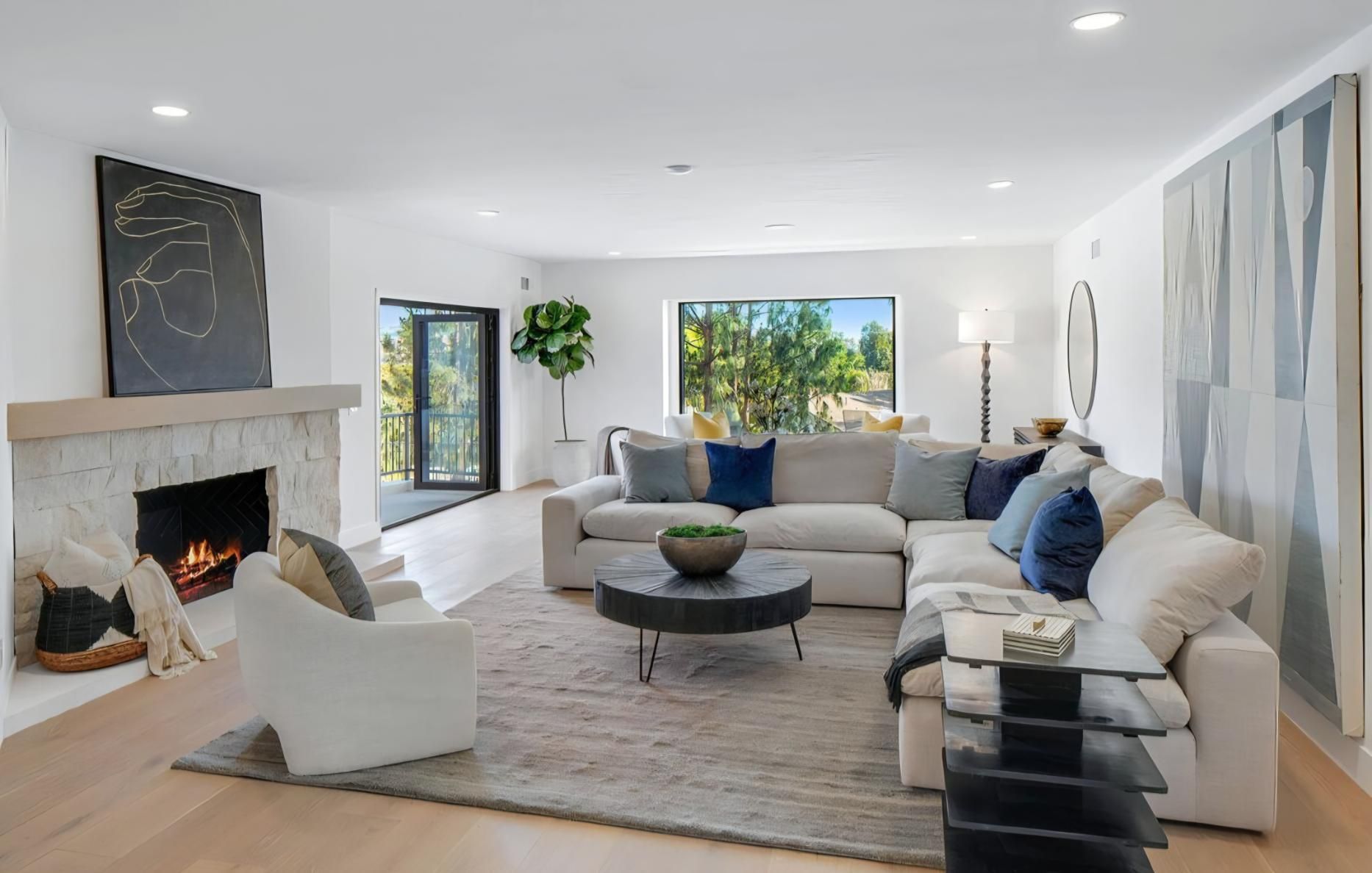 Bright living room with white sectional, fireplace, large window, and abstract wall art