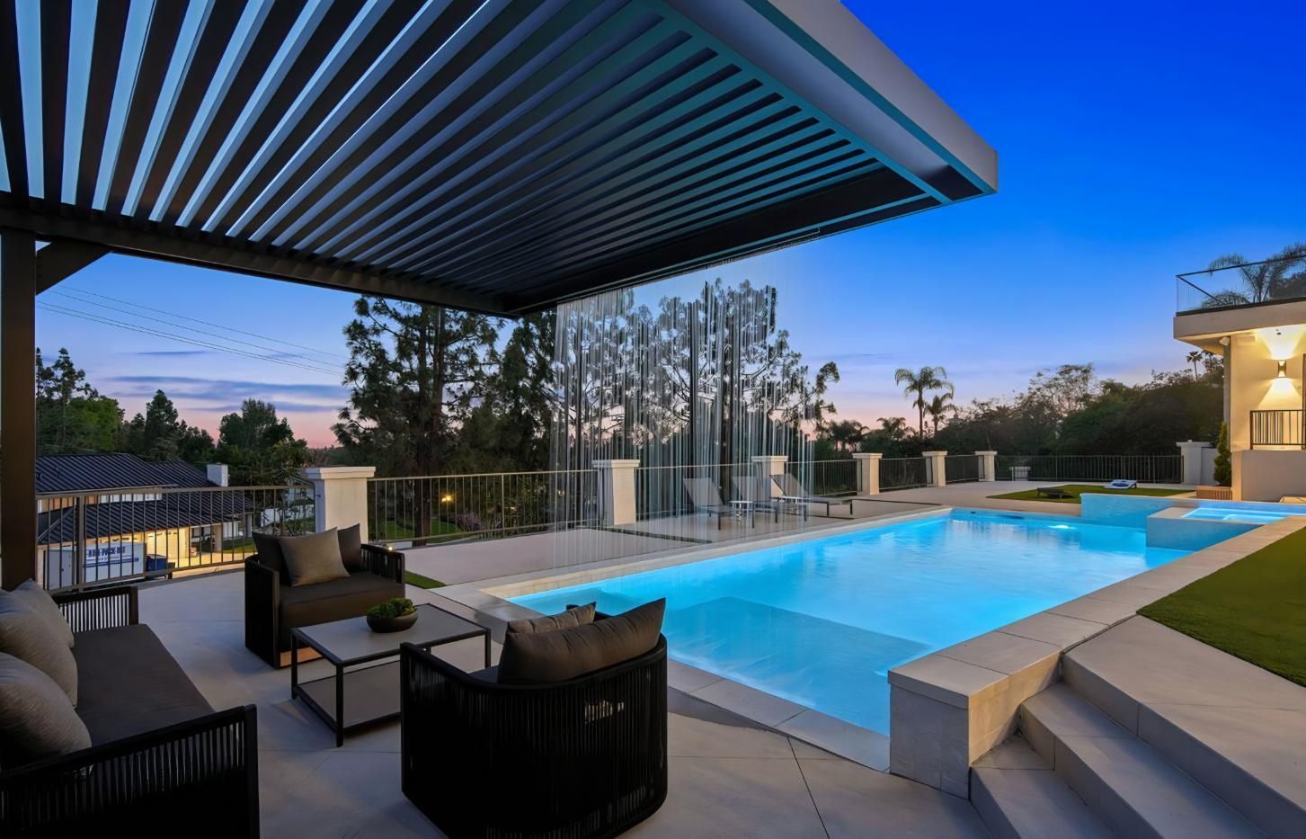 Modern backyard pool at dusk with lounge chairs, pergola, and blue water reflecting the sky