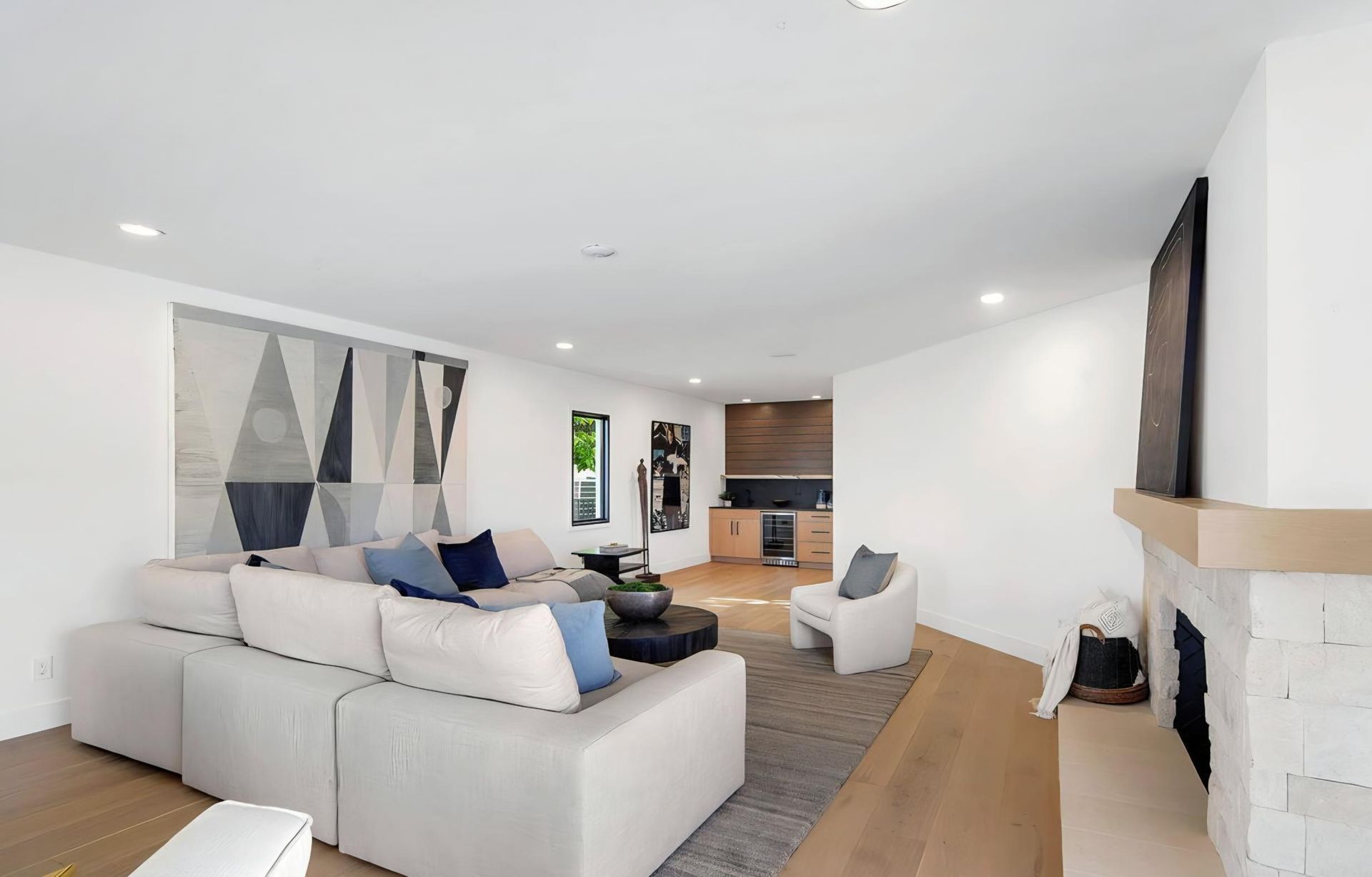 Bright living room with beige sectional, abstract wall art, wood floor, fireplace, and open kitchen area
