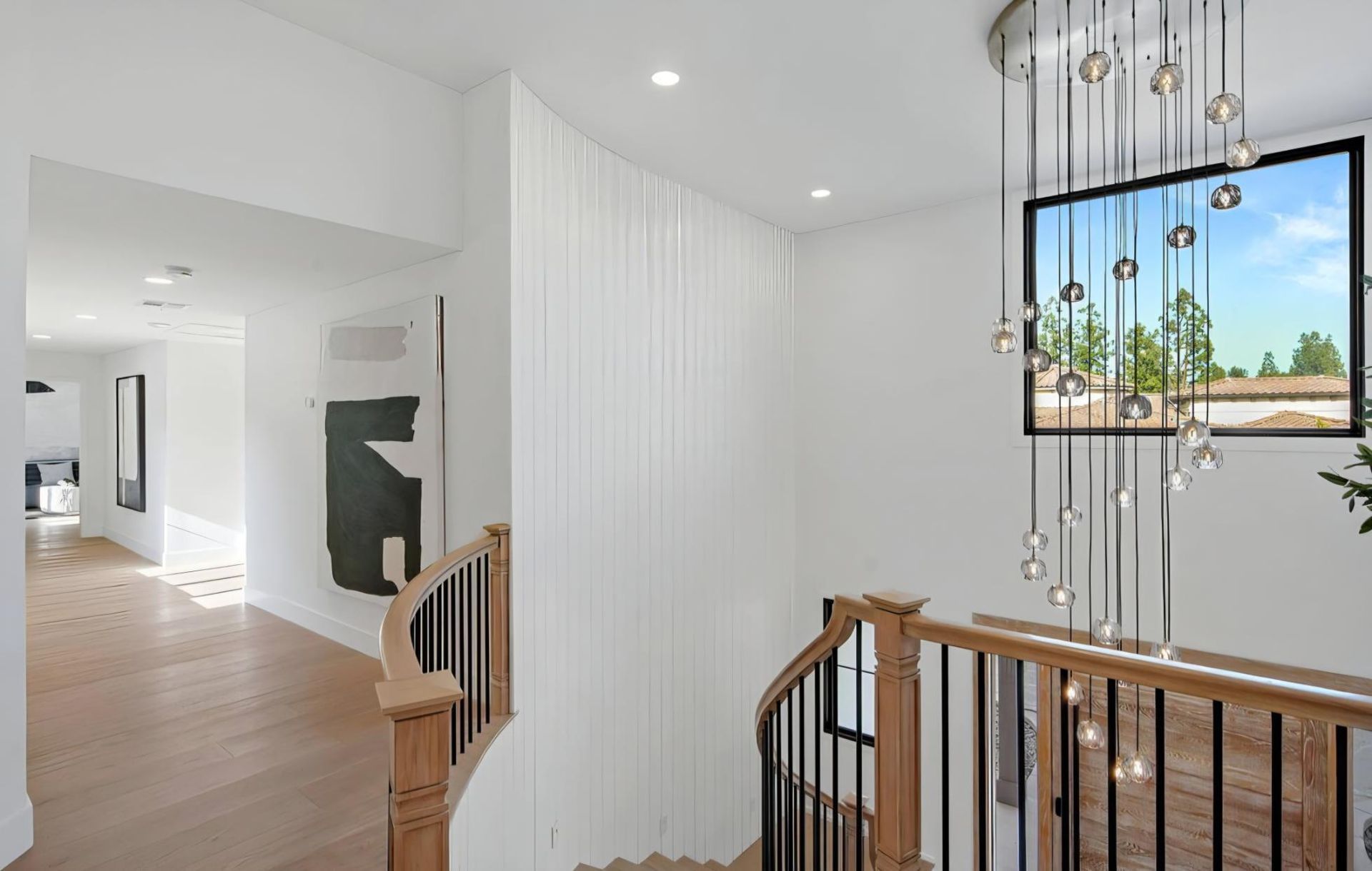 Bright stair landing with white paneled walls, wood railing, and a large window overlooking palm trees.