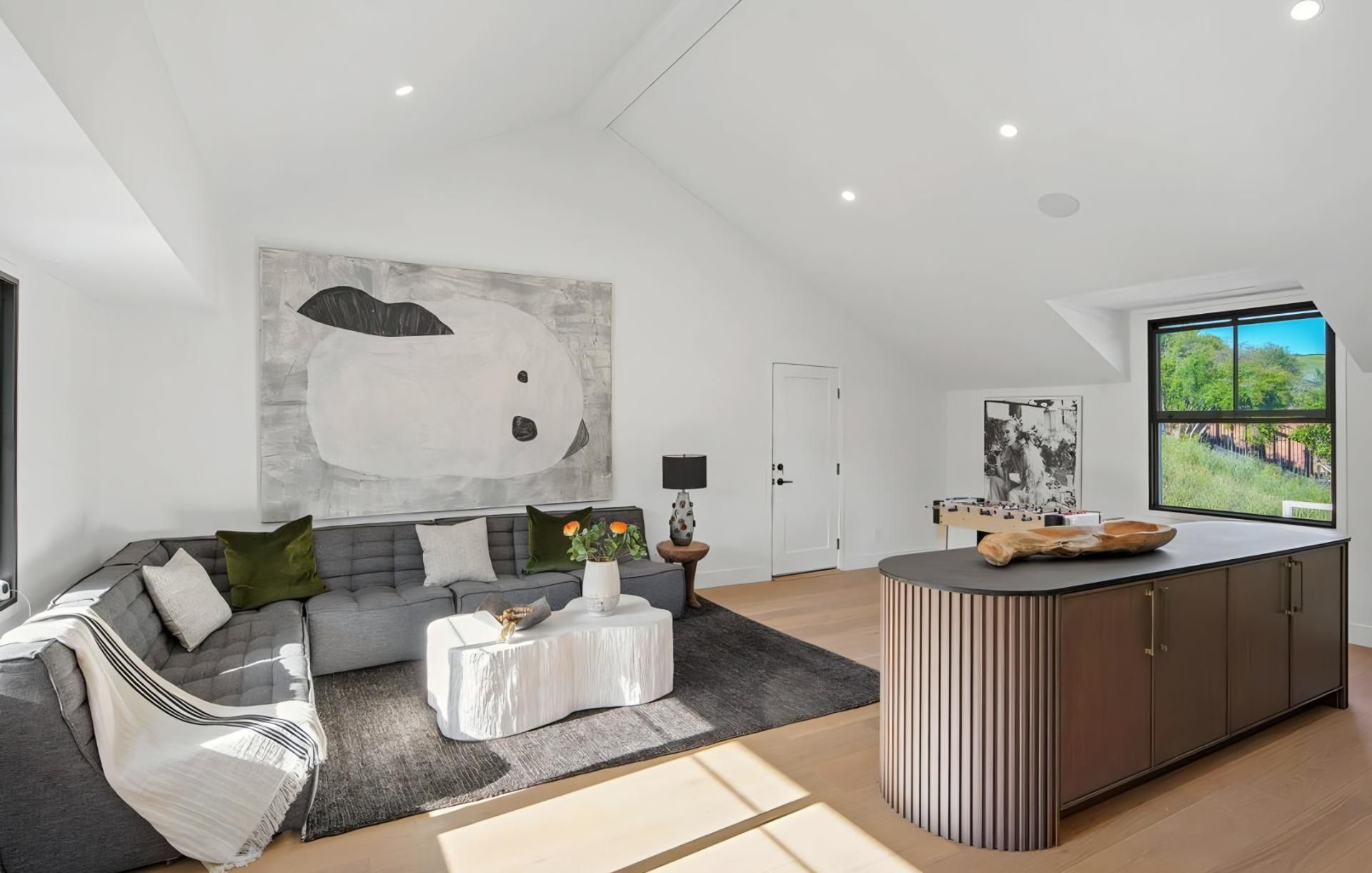 Bright modern living room with sectional sofa, abstract wall art, and kitchen island by a window