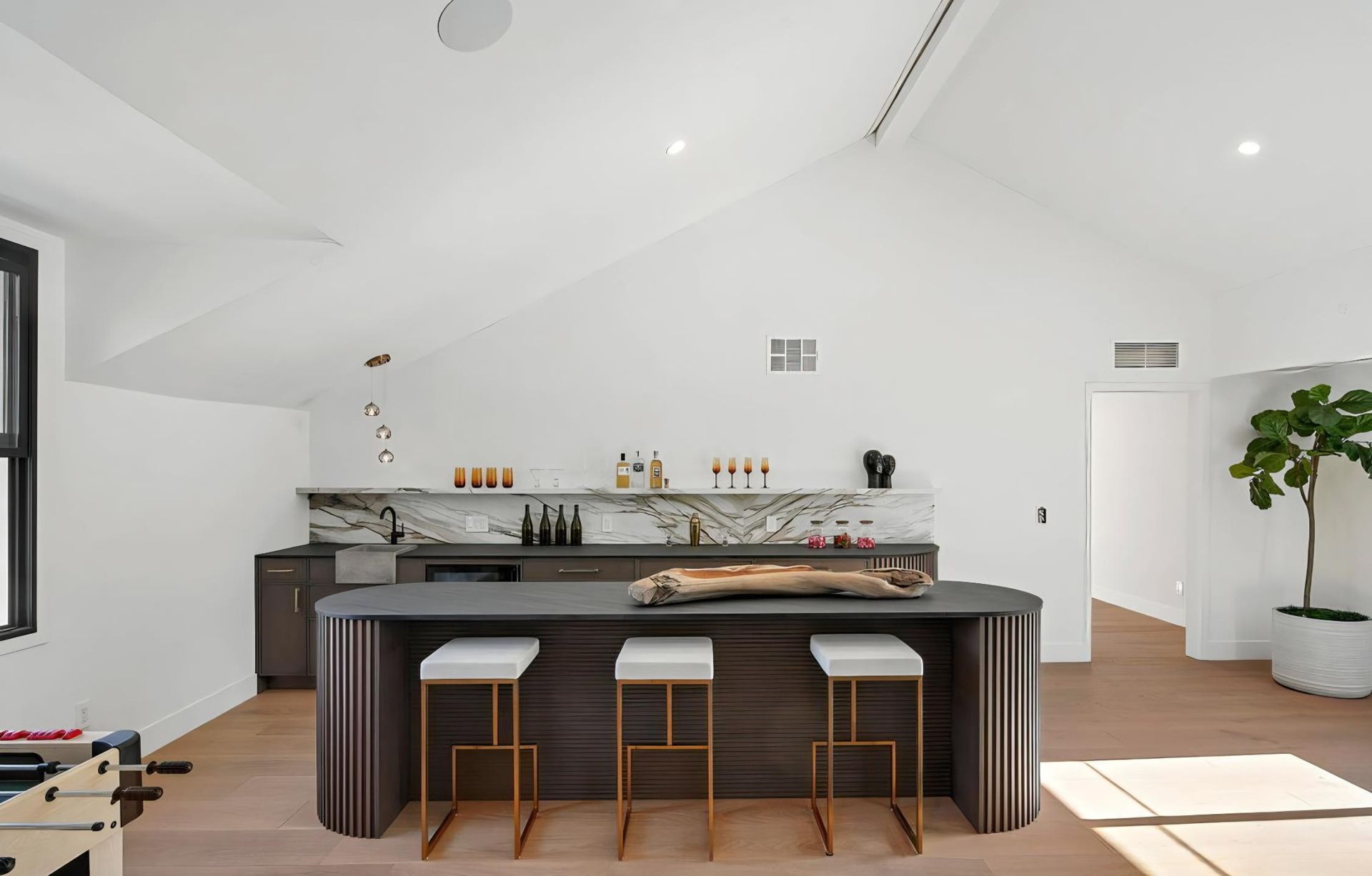 Bright minimalist kitchen with dark island, three stools, wood floors, and large windows