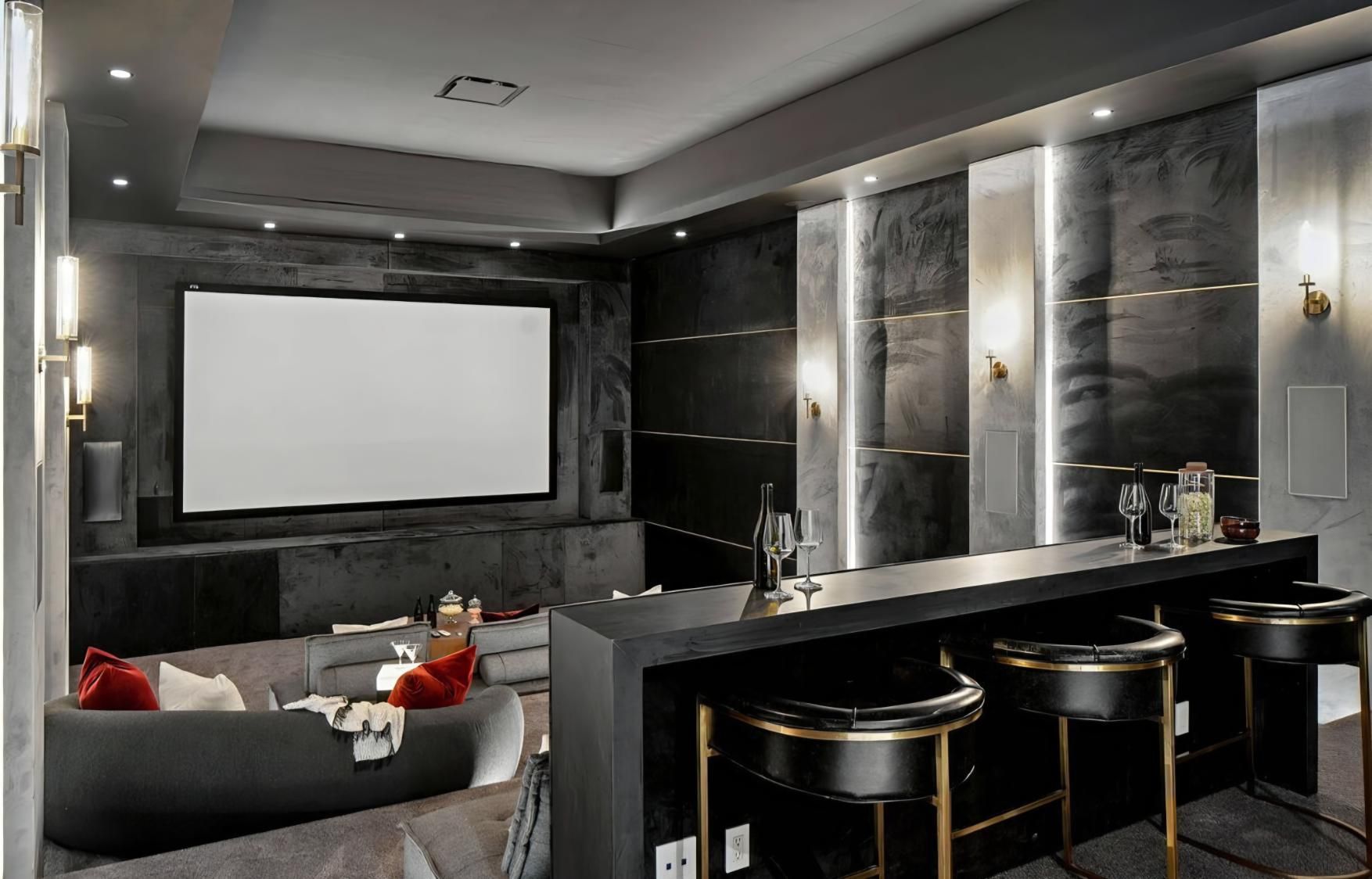 Luxurious home theater with a large screen, gray seating, and a dark bar with stools