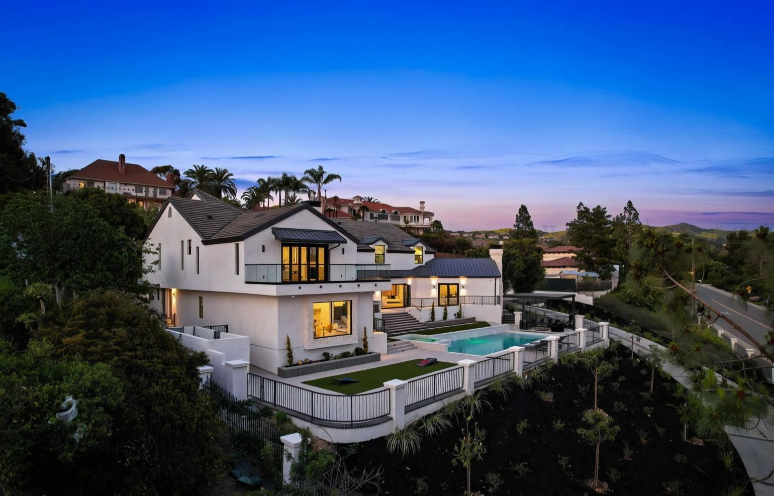 Modern hillside mansion at dusk with lit windows, pool, and city views