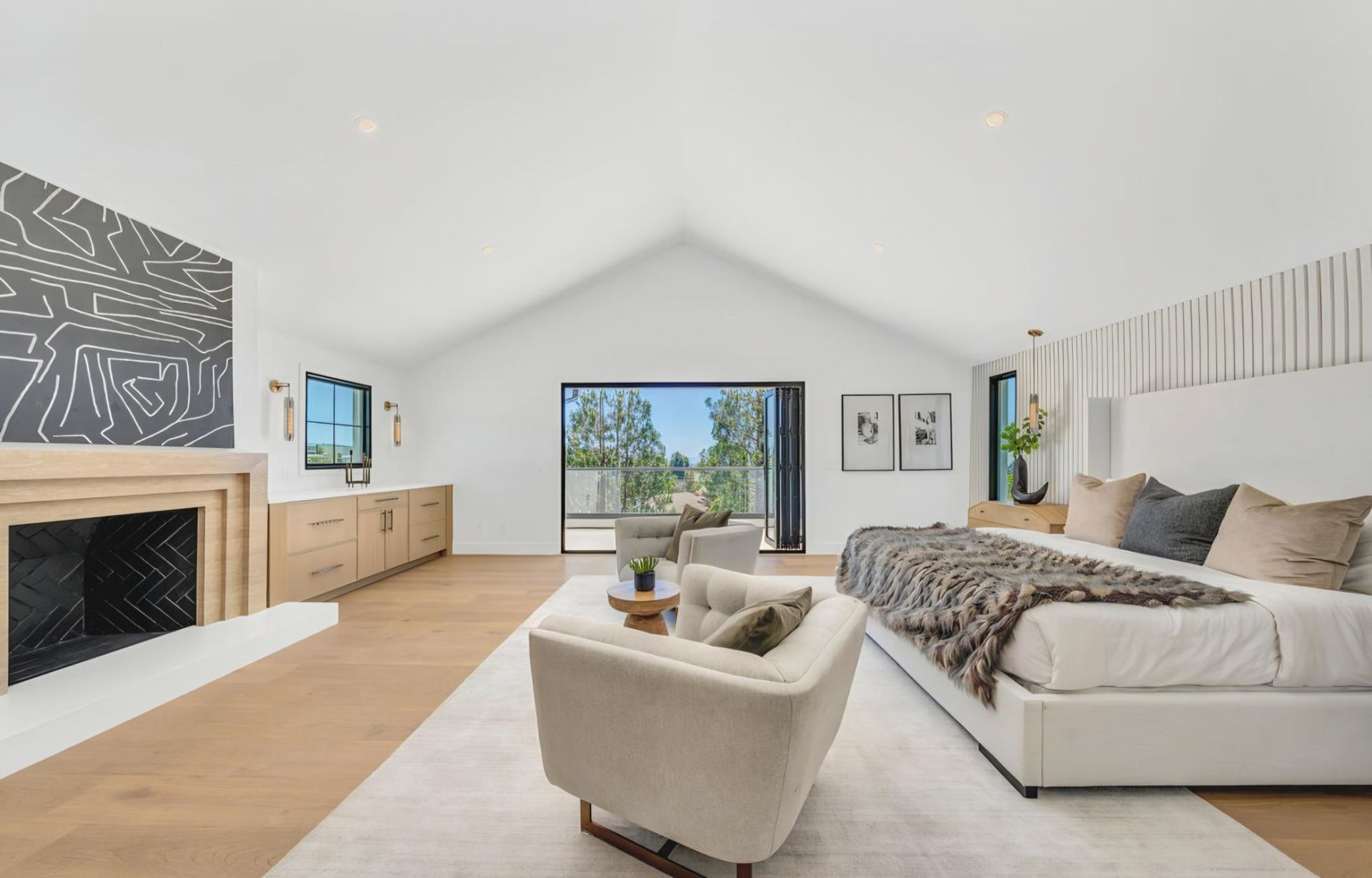 Bright, modern living room with a fireplace, sectional sofa, armchair, and large windows overlooking trees