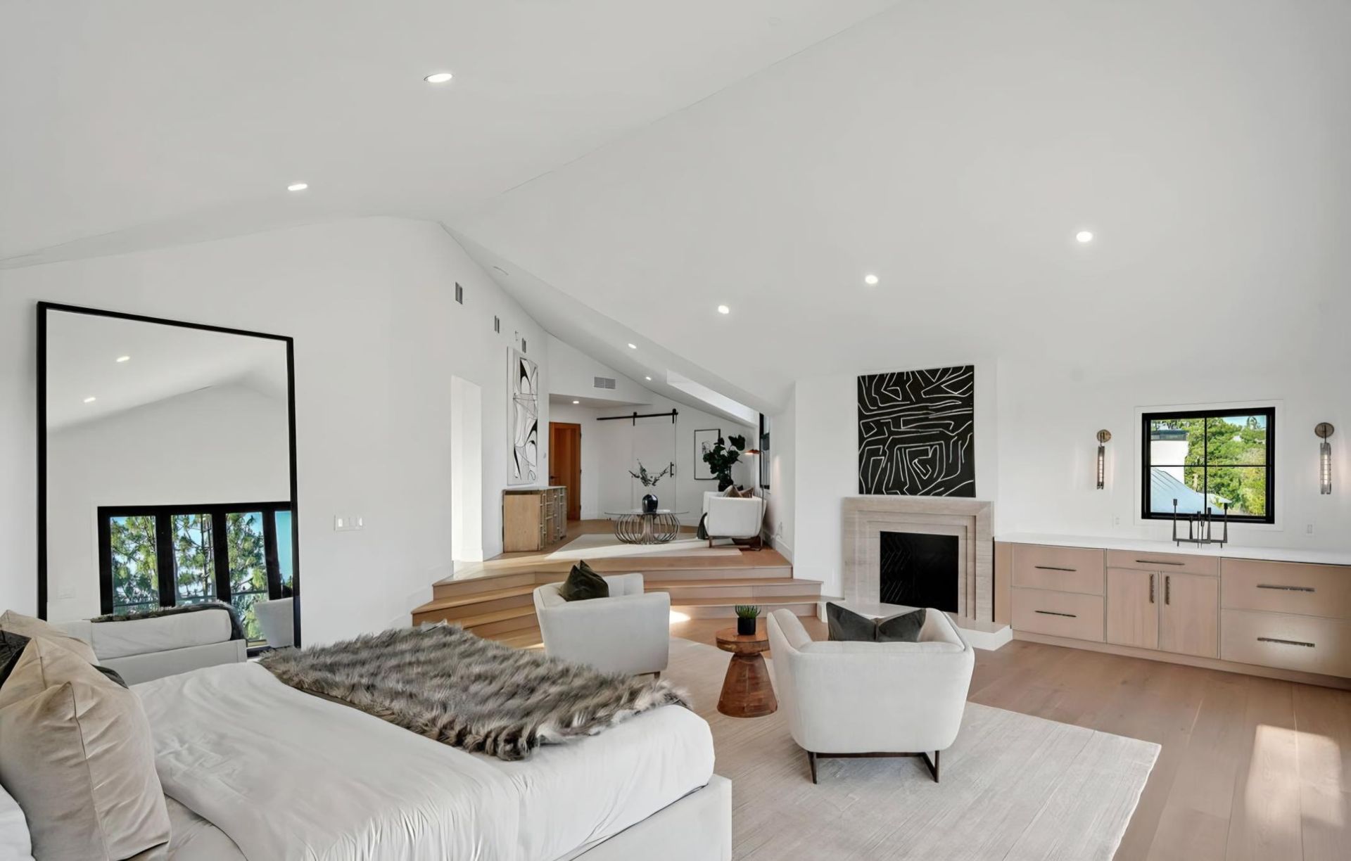 Bright modern living room with white walls, fireplace, staircase, and large windows