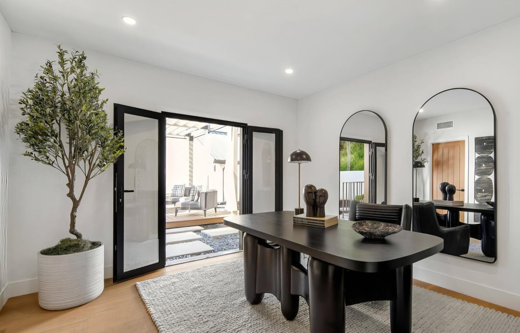 Modern dining room with black table, arched mirrors, and open French doors to a patio