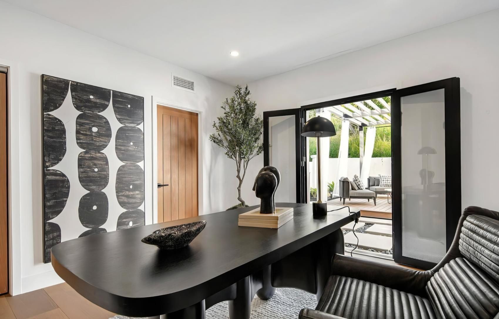 Modern dining room with black table, striped chairs, abstract wall art, and open glass doors to a patio