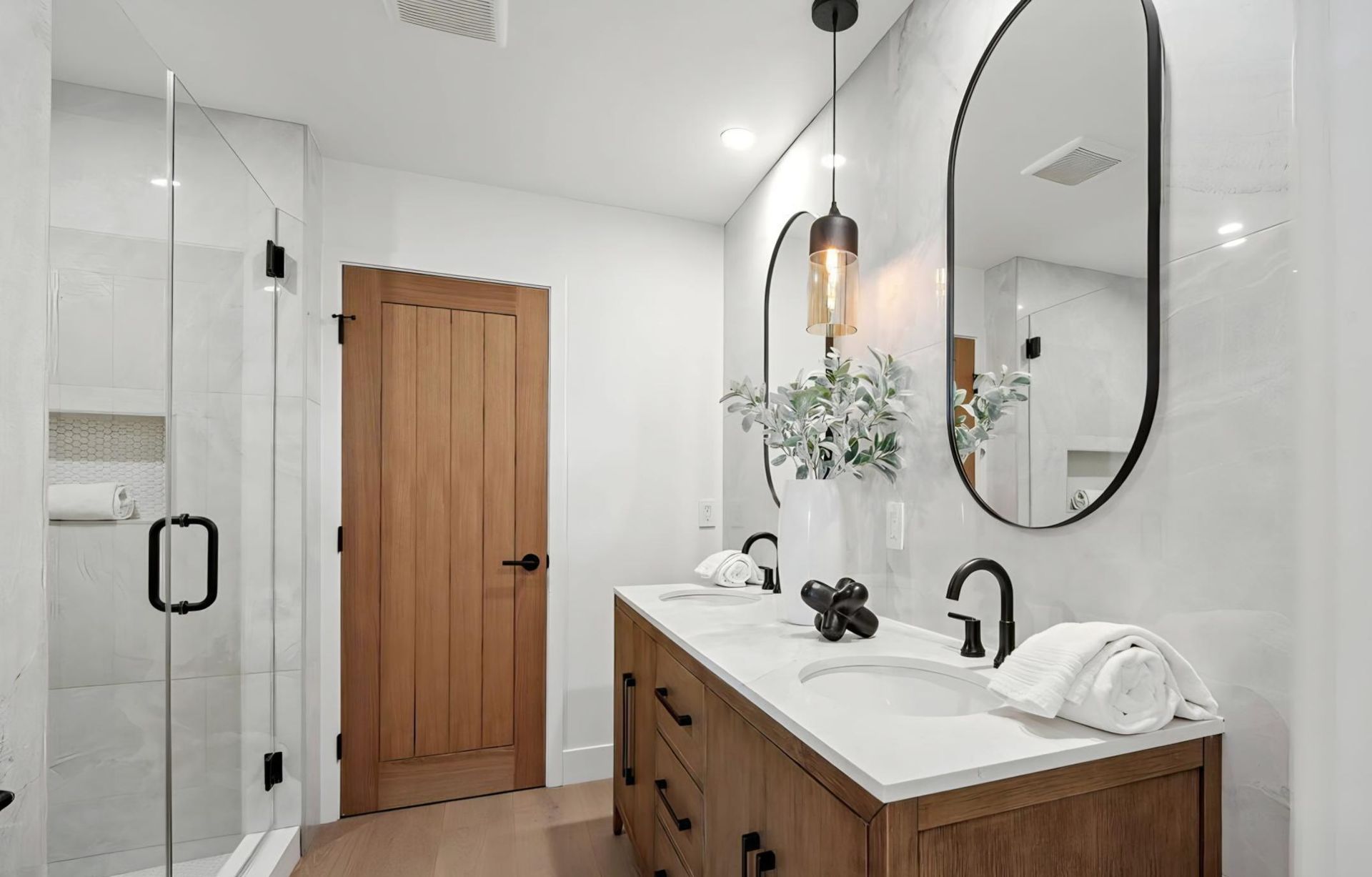 Modern bathroom with wood vanity, round mirror, black fixtures, and shower glass door