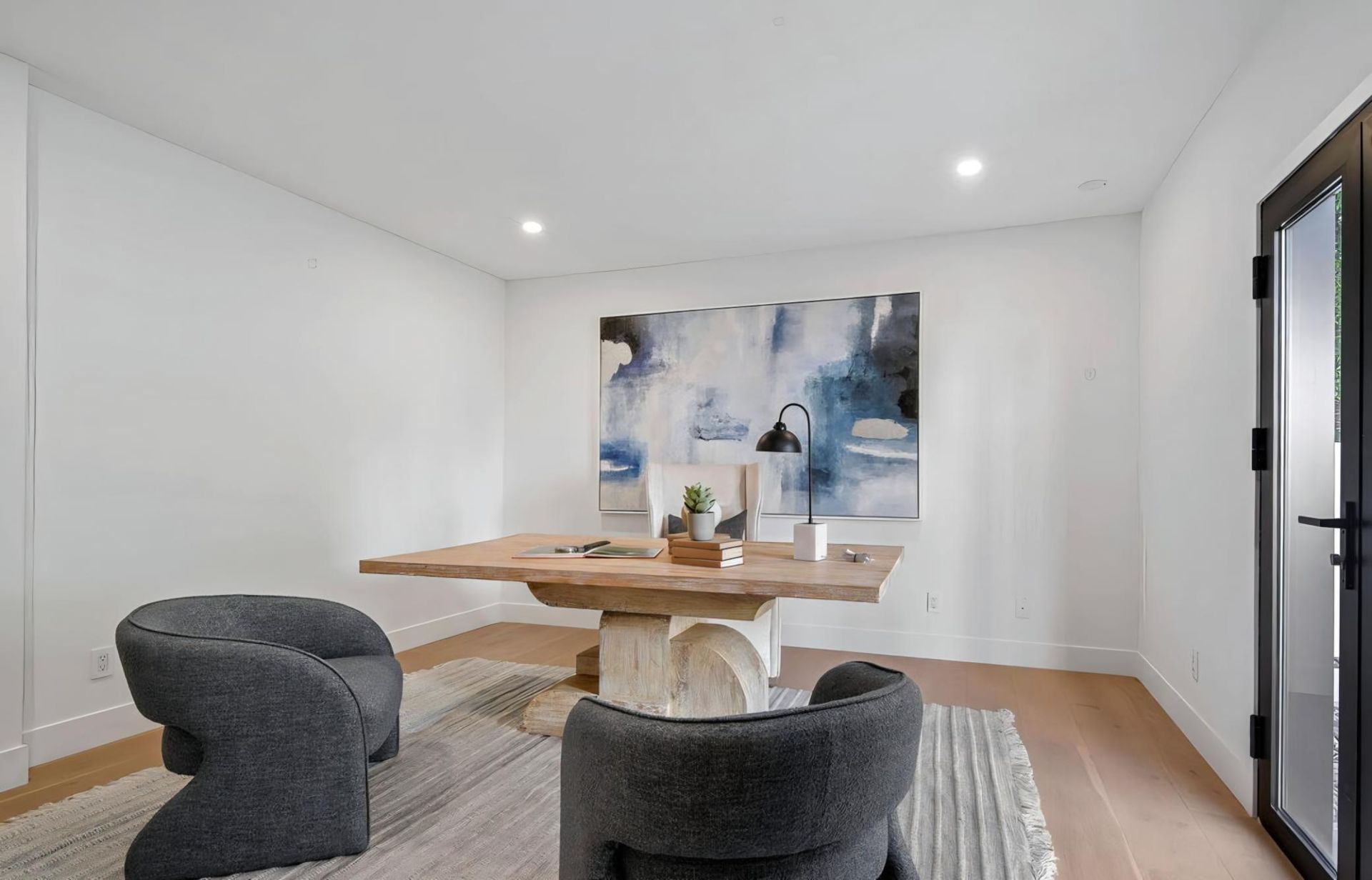 Modern dining room with a wooden table, dark chairs, large abstract art, and light wood floors