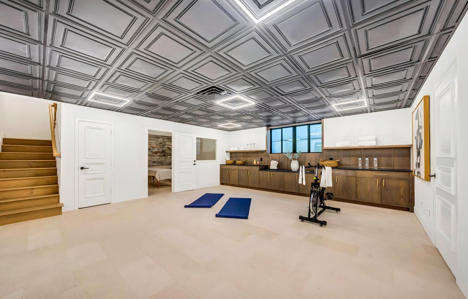 Finished basement gym with patterned ceiling, beige carpet, wooden cabinets, blue mats, and exercise bike