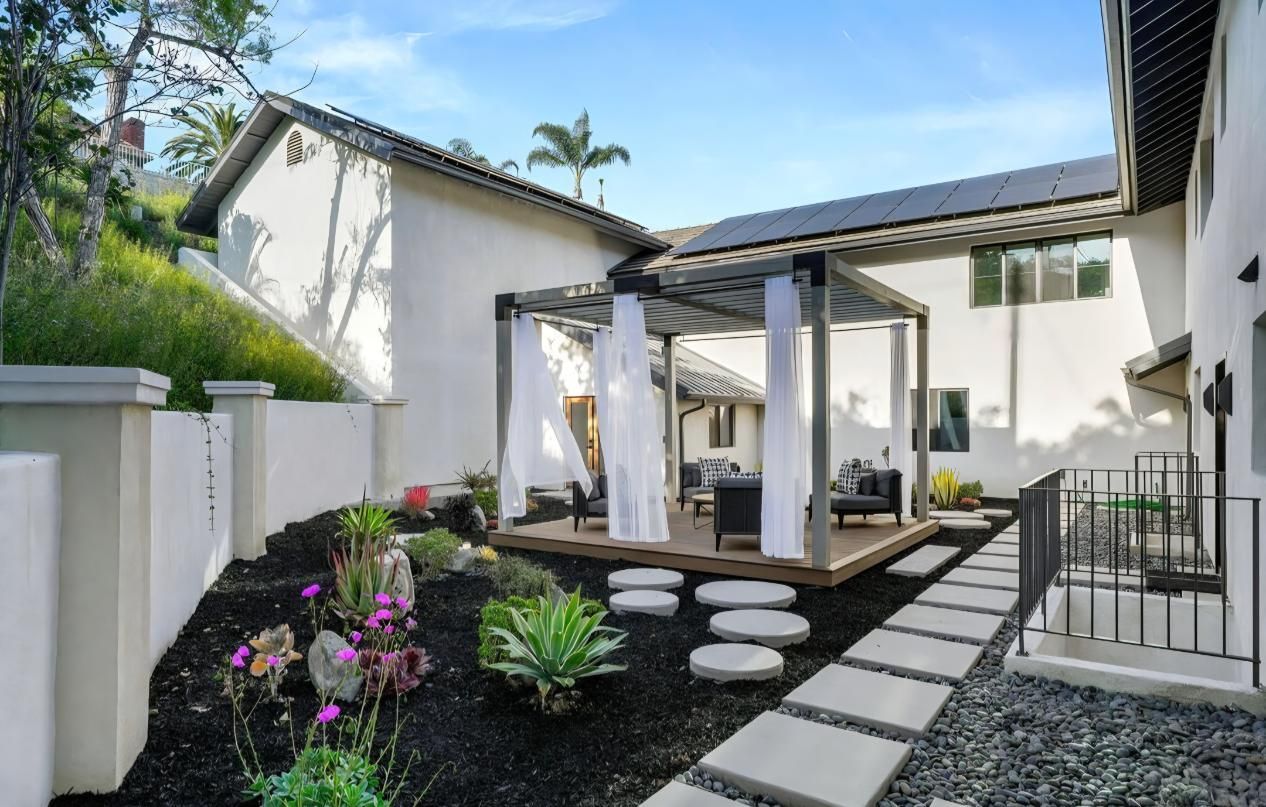 Modern backyard patio with white stone path, pergola, stepping stones, and purple flowers