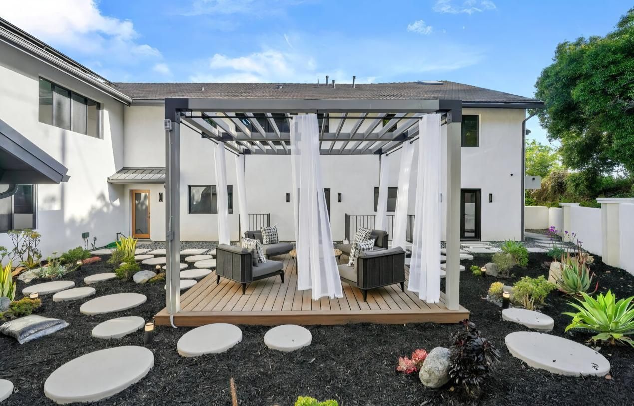 Backyard pergola with white curtains, outdoor seating, and stone stepping pads in a landscaped garden