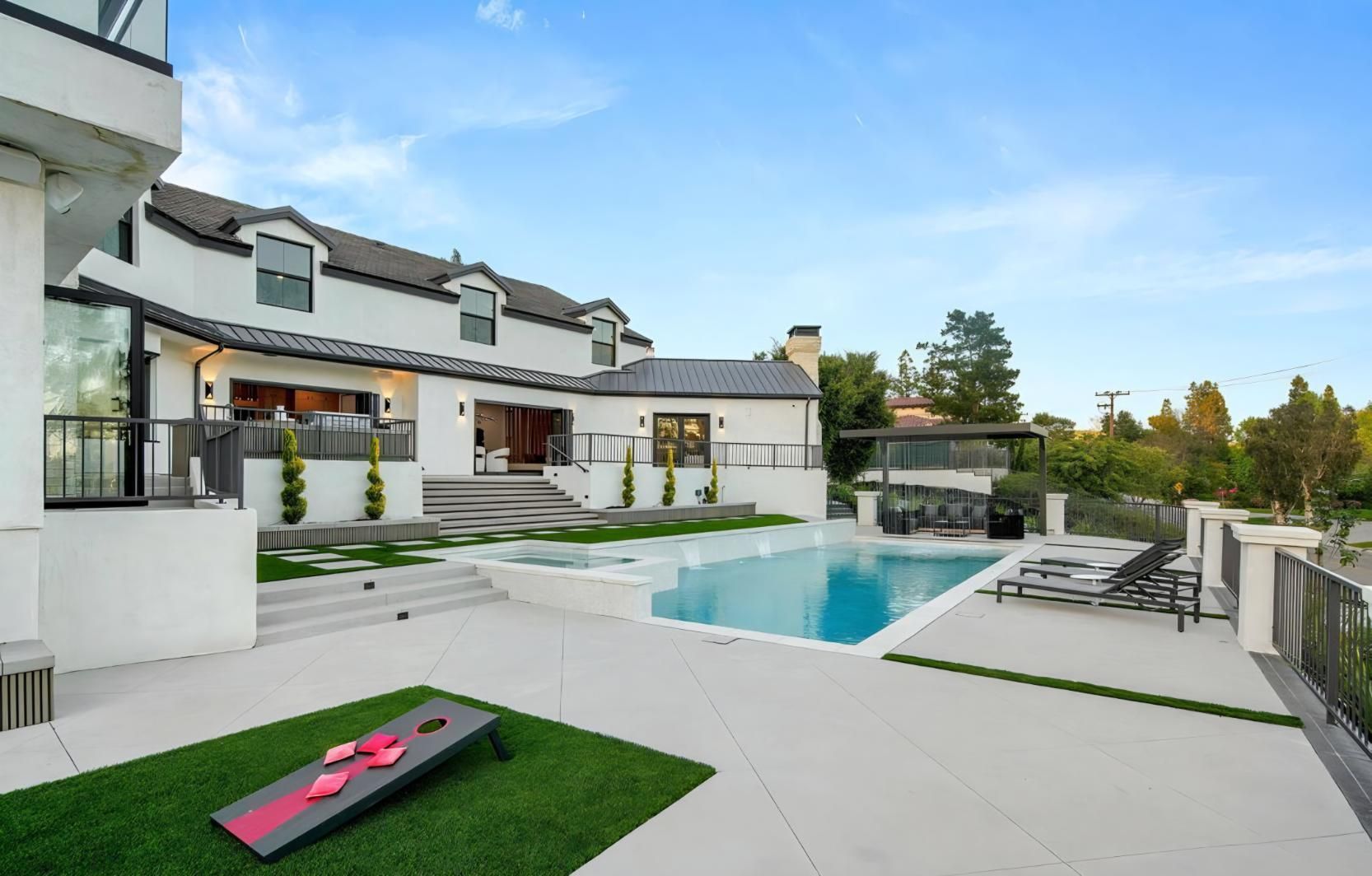 Modern luxury house with a turquoise pool, lounge chairs, and white patio at sunset