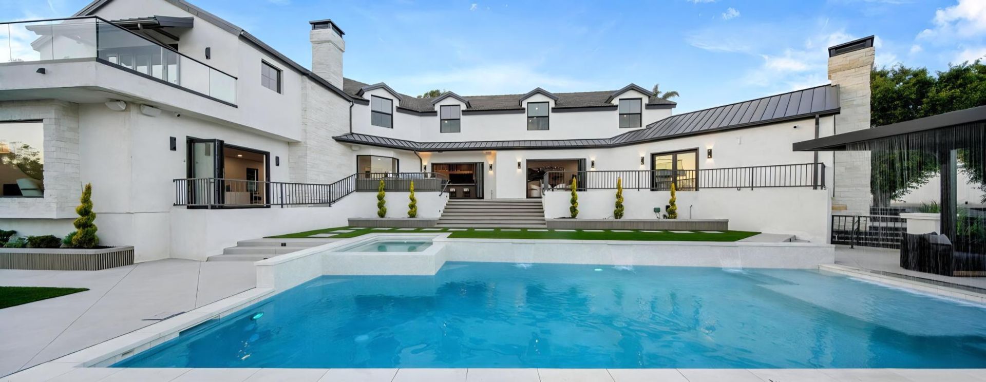 Luxury home backyard with a swimming pool, patio seating, and white exterior walls.