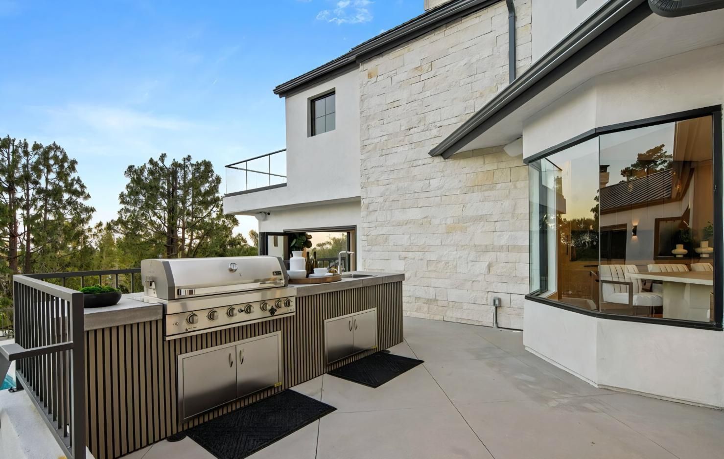 Modern house patio with outdoor kitchen, grill, and seating on a stone terrace