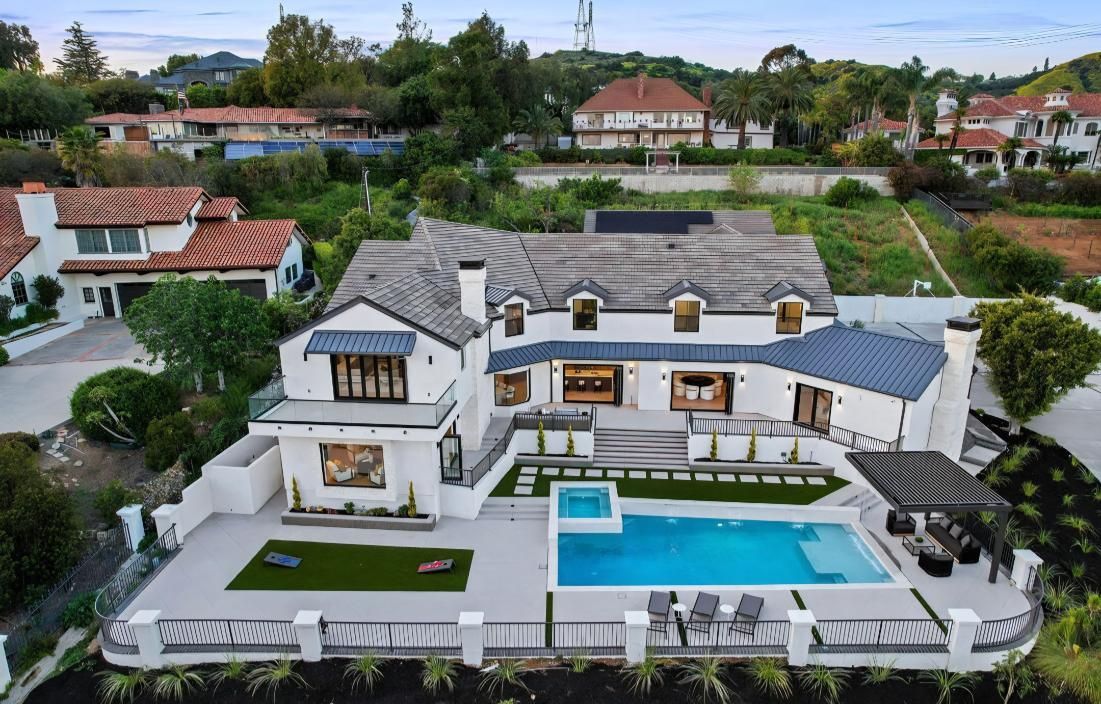 Aerial view of a large modern house with a pool and landscaped yard in a hillside neighborhood