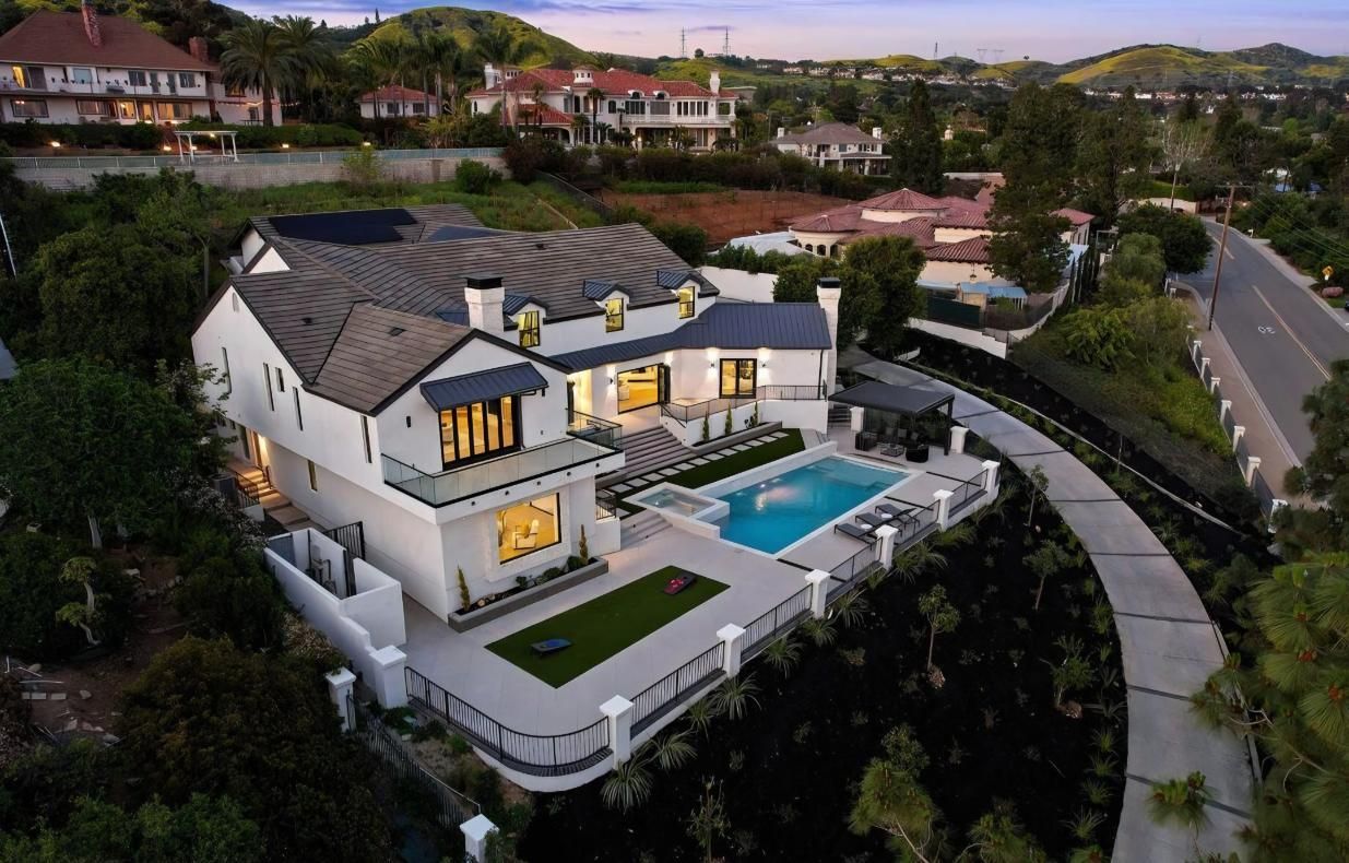 Aerial view of a luxury hillside villa with a pool, terrace lights, and winding road at dusk