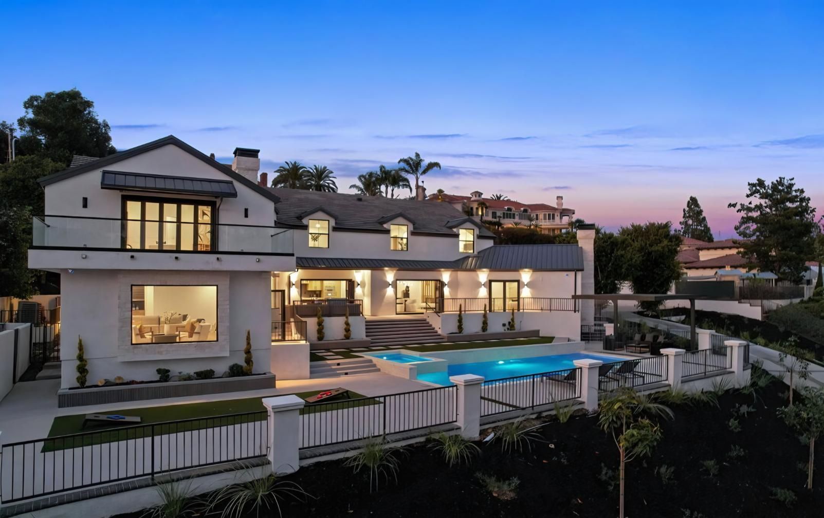 Luxury hillside home at dusk with lit windows, pool, and ocean view