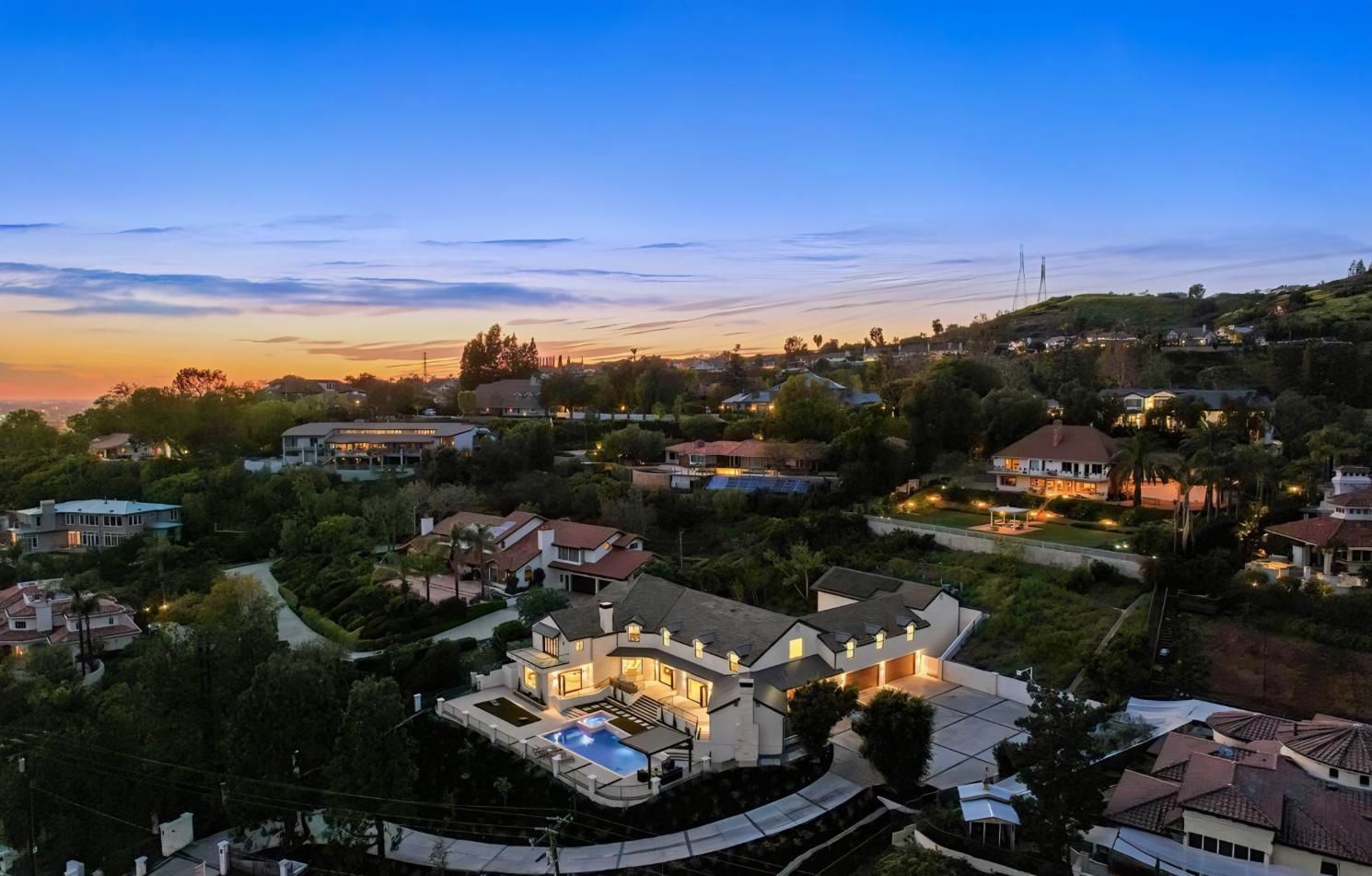 Sunset over a hillside neighborhood with houses, trees, and a glowing sky